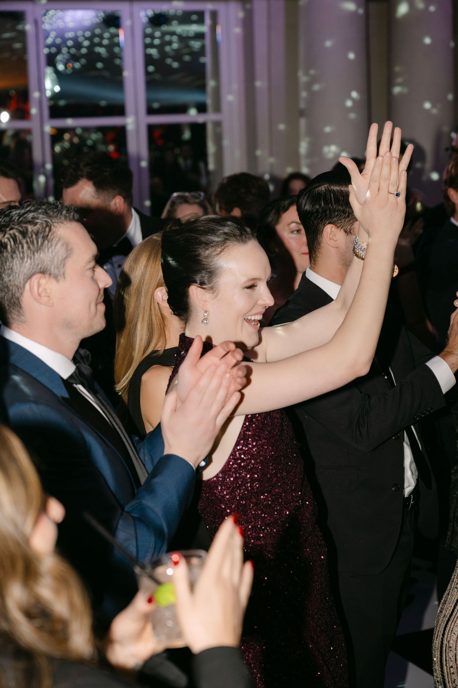 Woman in burgundy sequin dress dancing joyfully with hands raised at elegant evening event.