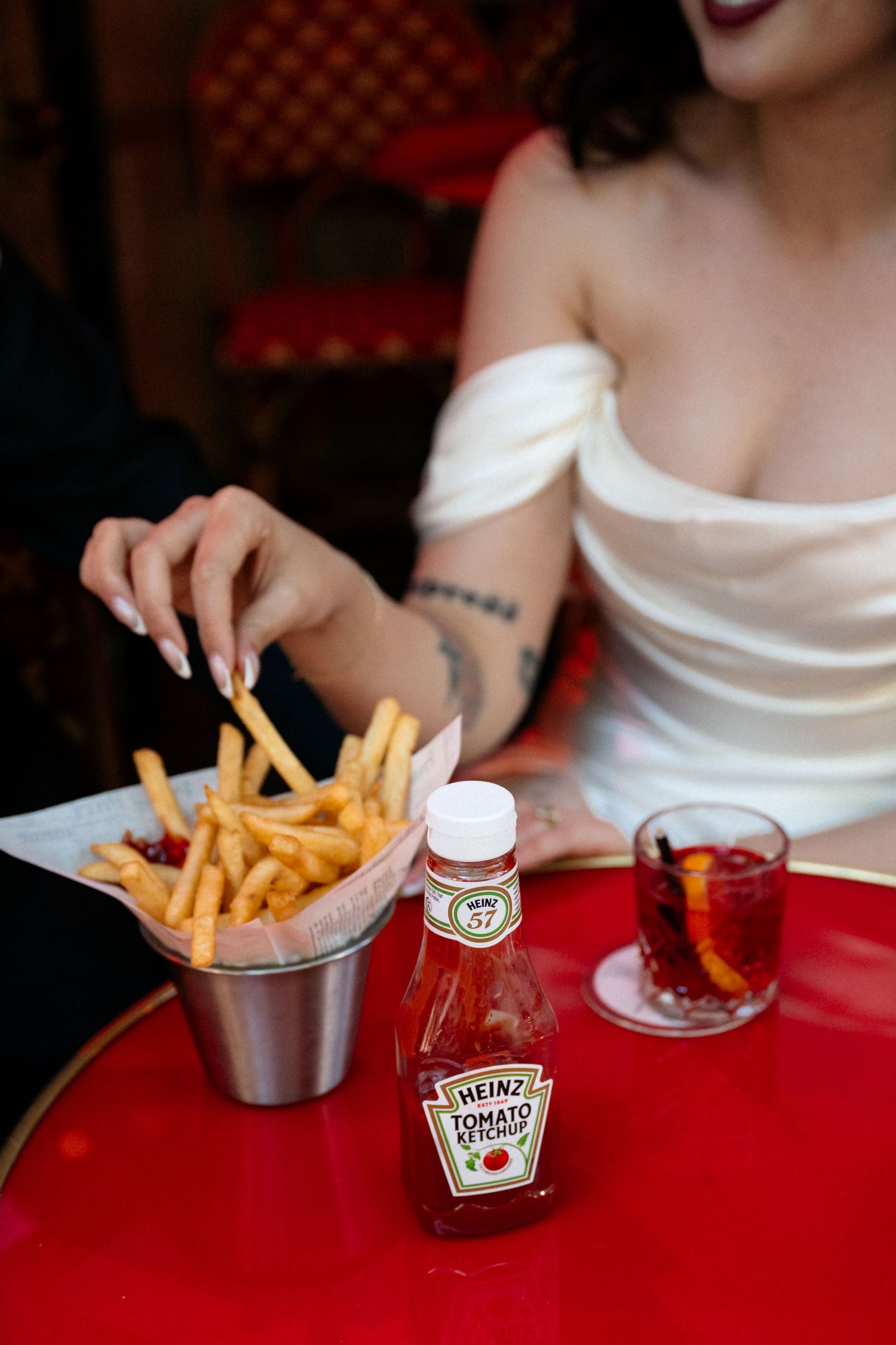 Bride in white off-shoulder gown eating french fries with Heinz ketchup.