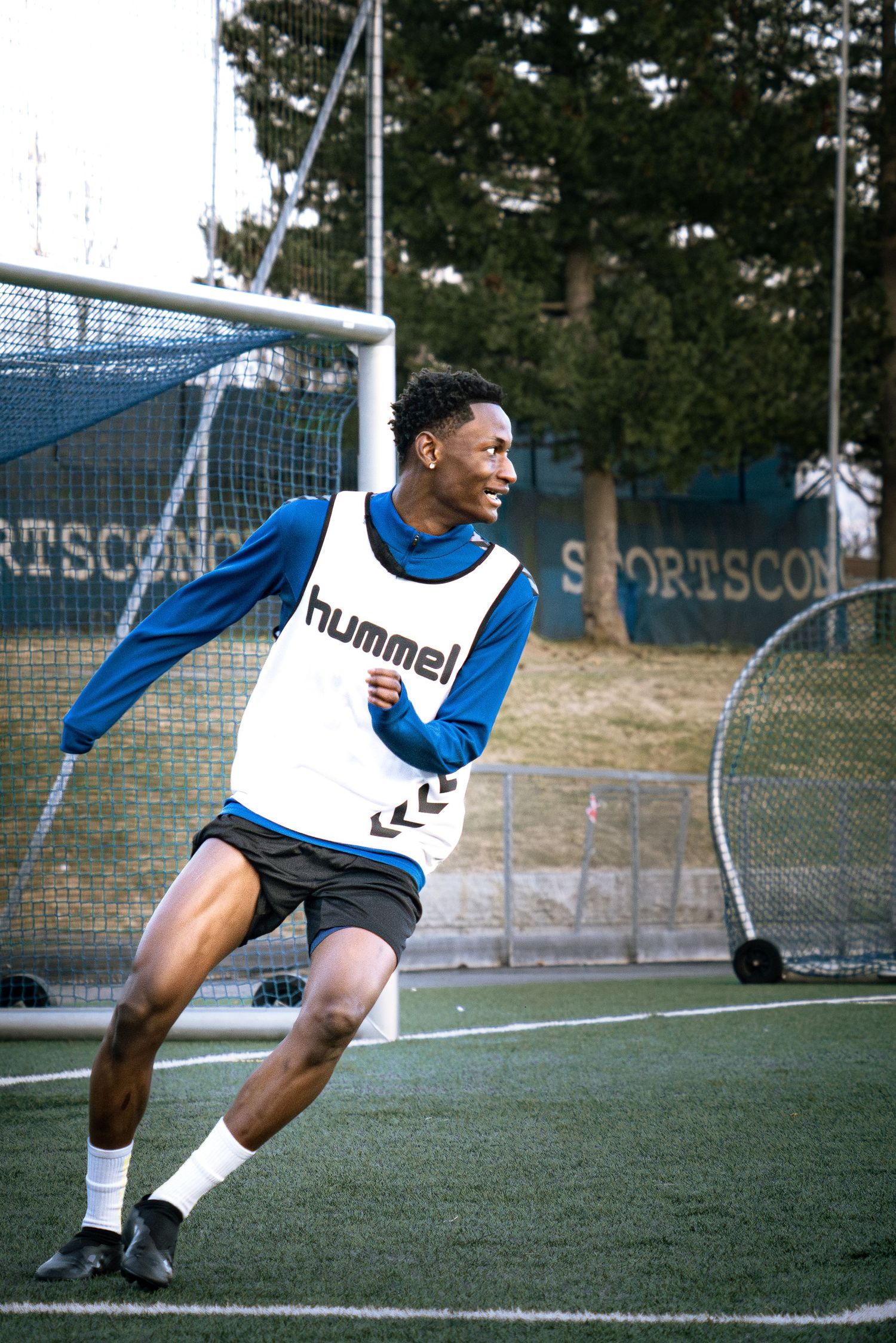 Young male soccer player in Hummel bib sprinting on artificial turf field during training session.