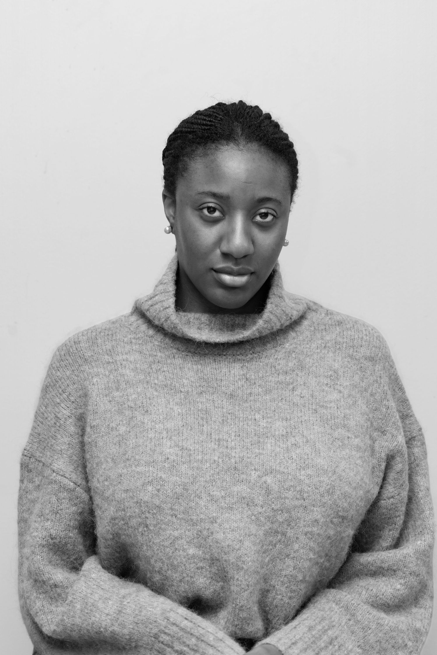Person in grey turtleneck sweater poses with subtle smile against white backdrop.