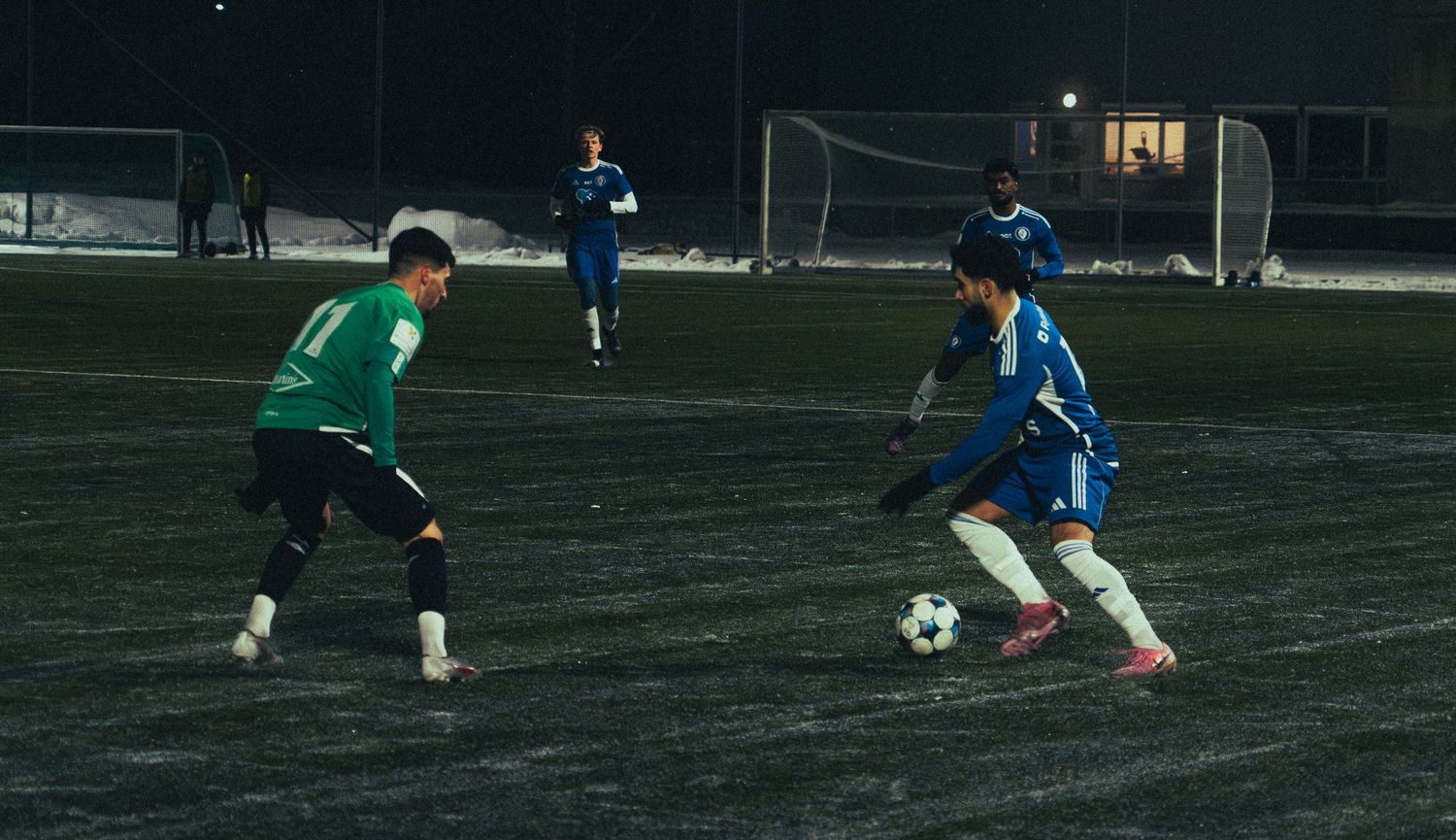 Soccer players compete on dark field during nighttime match.