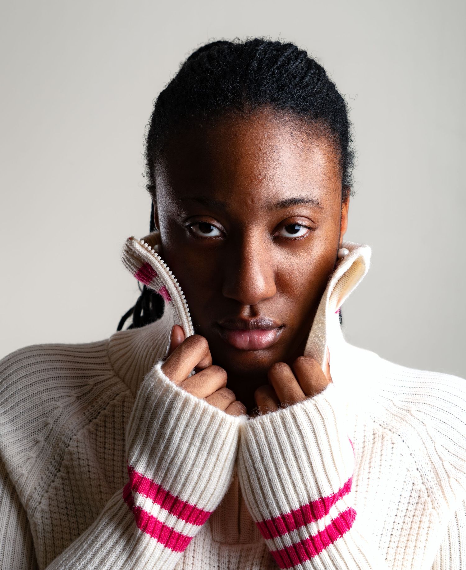 Person in cream sweater with pink stripes shows playful expressions in minimalist portrait series.