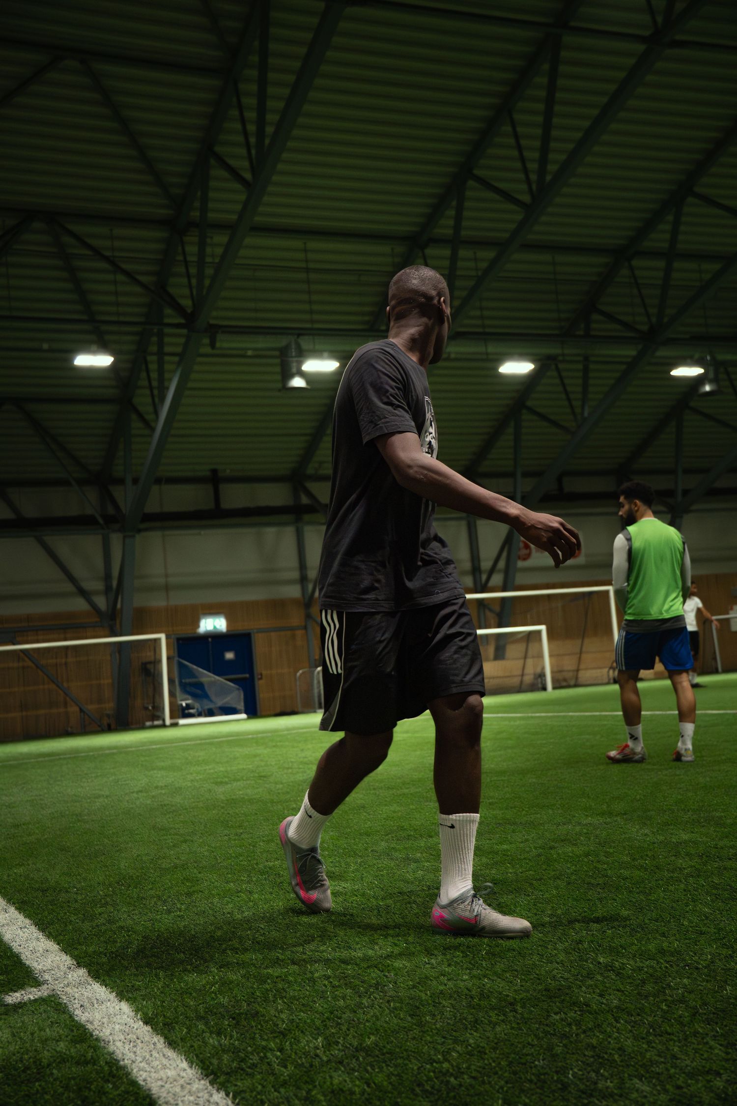 Players practicing soccer on an indoor artificial turf field under bright lights in a sports facility.