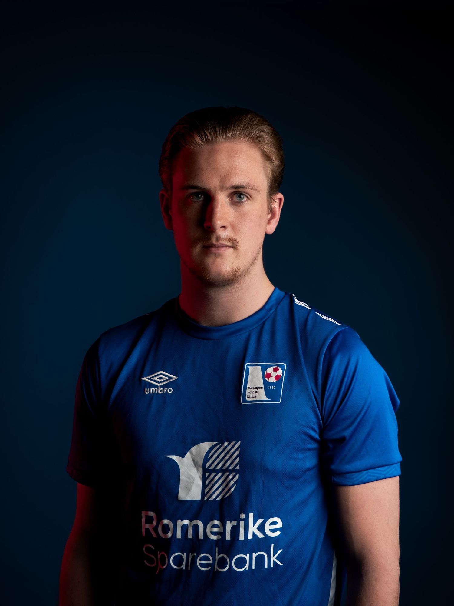 Sports player wearing blue Romerike Sparebank team jersey in professional studio portrait.