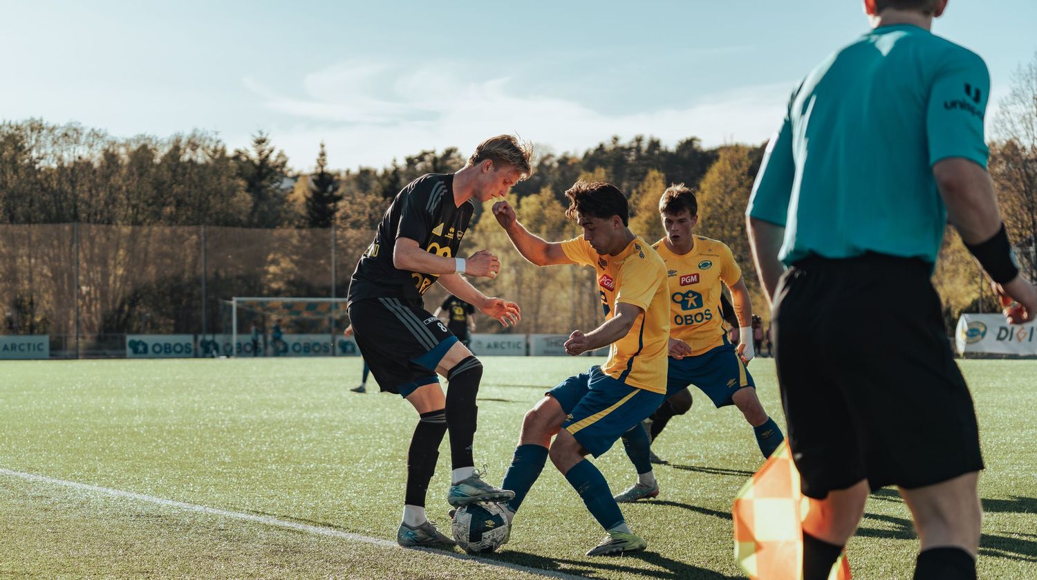 Soccer players in black and yellow jerseys compete for the ball on a green field during an outdoor match.