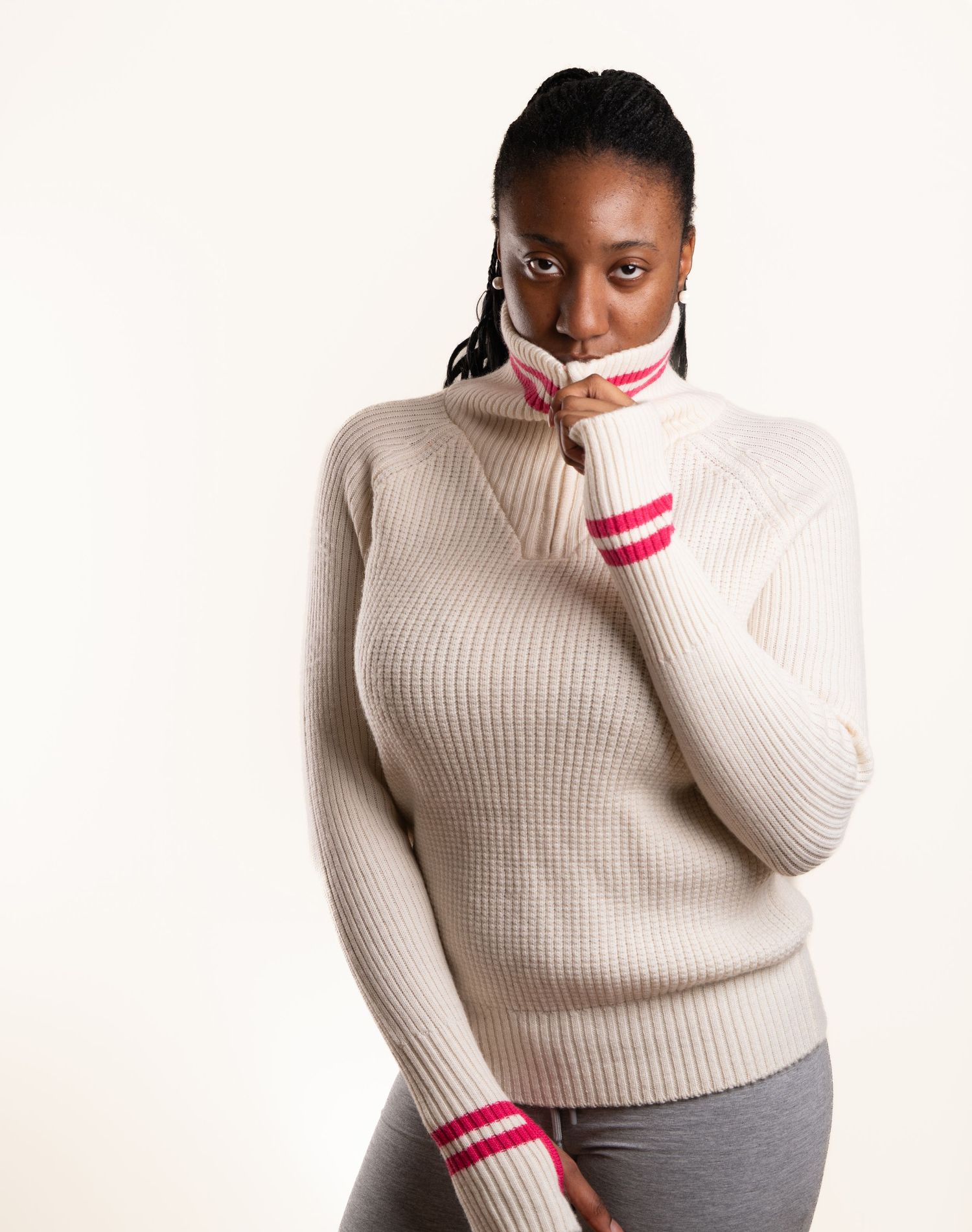 Person in cream sweater with pink accents poses against white background in fashion portrait series.