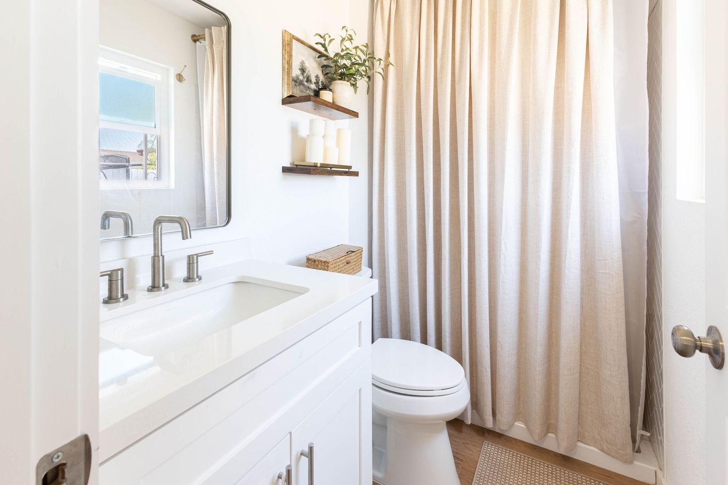 Modern white bathroom with undermount sink vanity, framed mirror, toilet, and beige linen shower curtain.