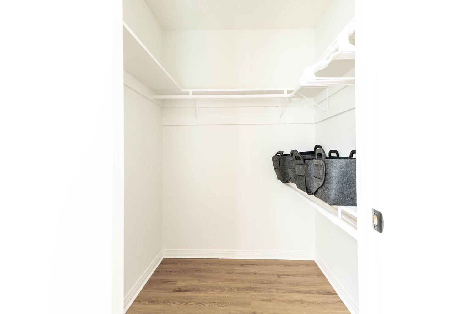 Spacious walk-in closet with white shelving, hanging rods, and light wood flooring.