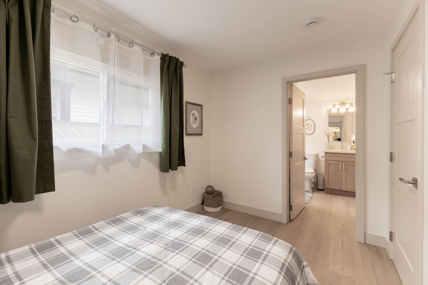 Cozy bedroom with plaid bedding, green curtains, and open door leading to en-suite bathroom.