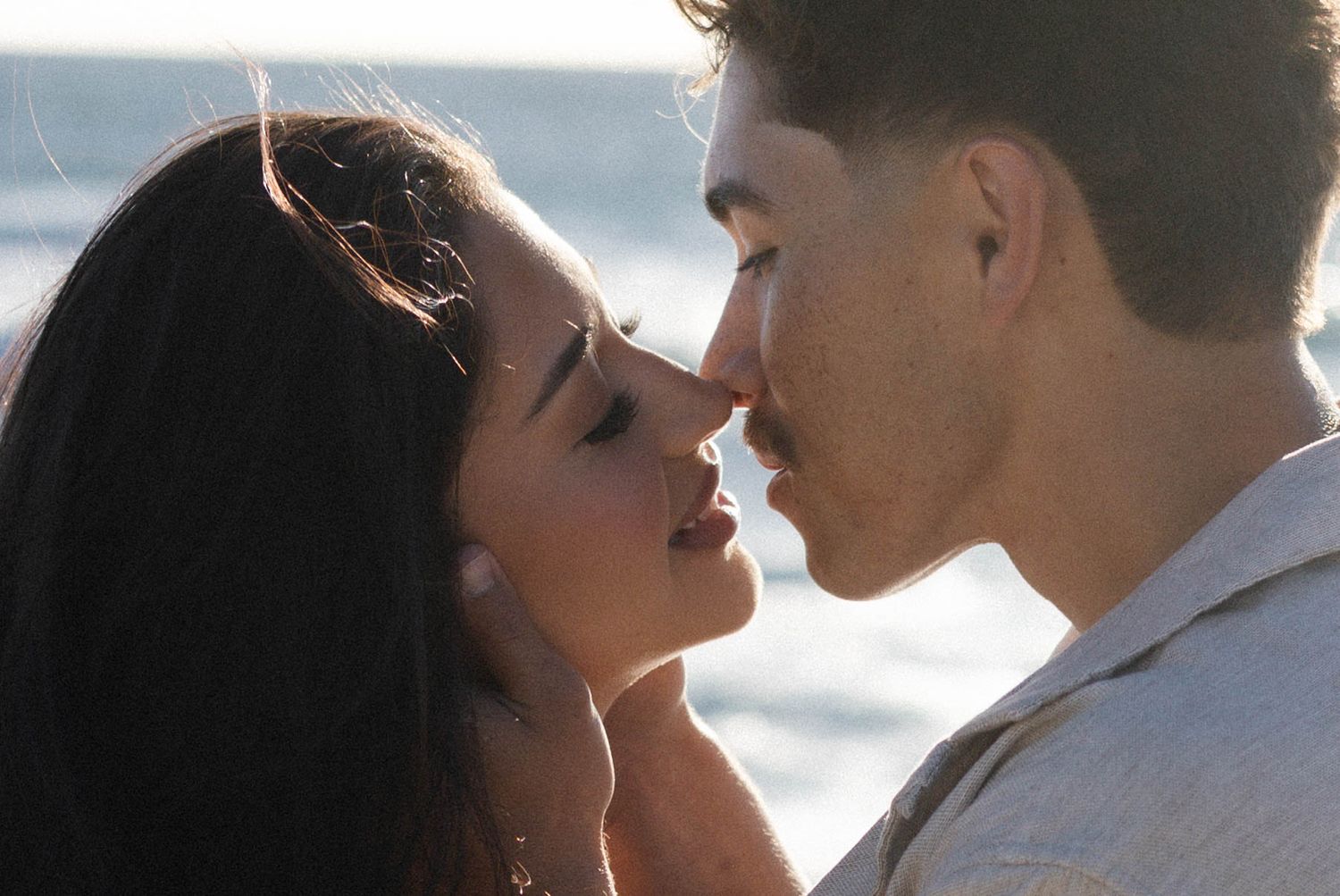 Couple sharing a romantic almost-kiss moment with ocean waves glowing in the background.