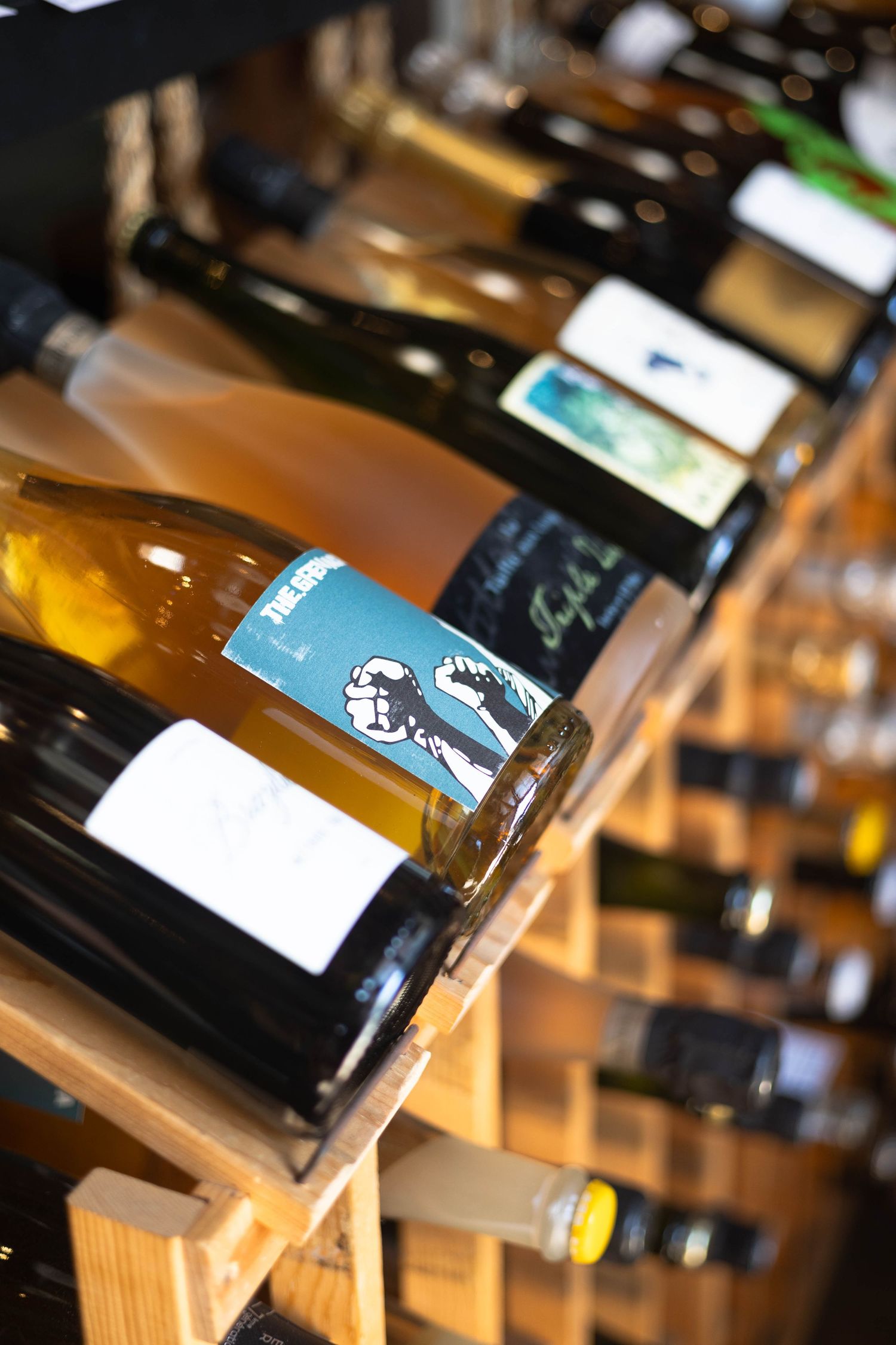 Wine bottles displayed on wooden rack in a wine shop, with visible labels and variety of white and red wines.