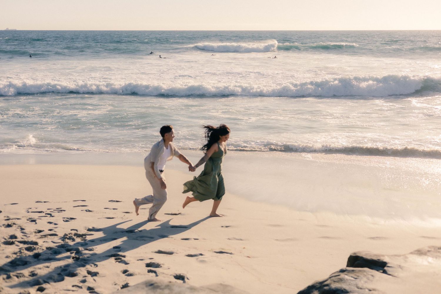 Joyful couple running and holding hands along the shoreline on a bright sunny beach.