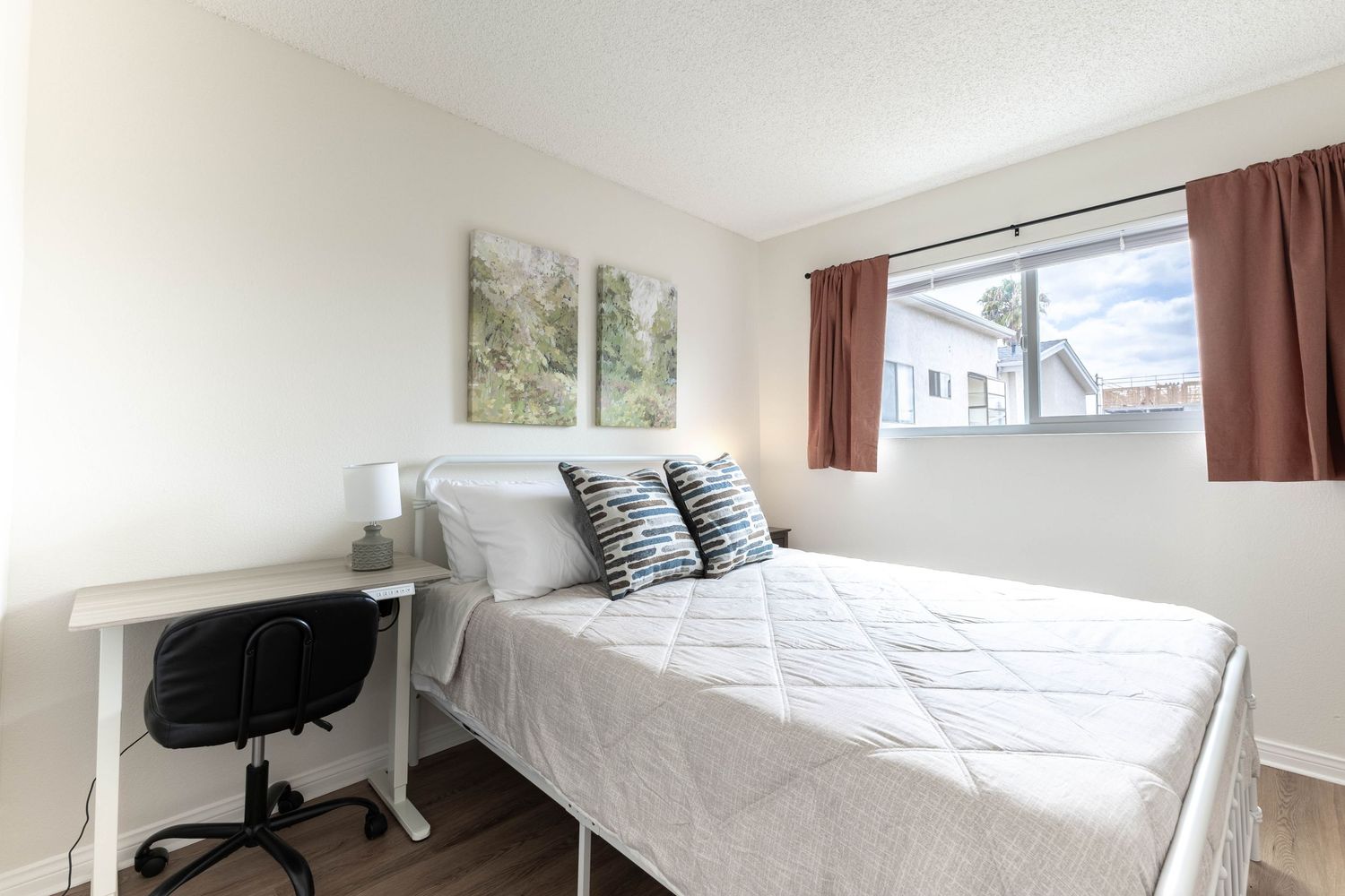 Cozy bedroom with desk, white bed, and reddish-brown curtains.