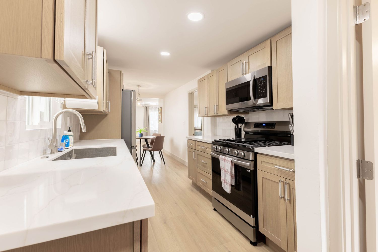 Modern kitchen with light wood cabinets, white quartz countertops, and stainless steel appliances.