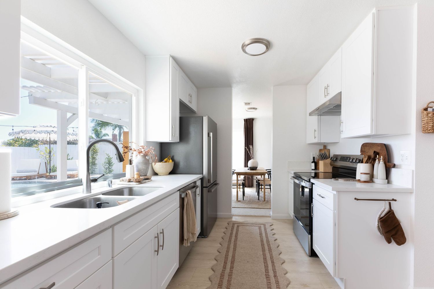 Modern galley kitchen with white cabinets, stainless steel appliances, farmhouse sink, and neutral runner rug.