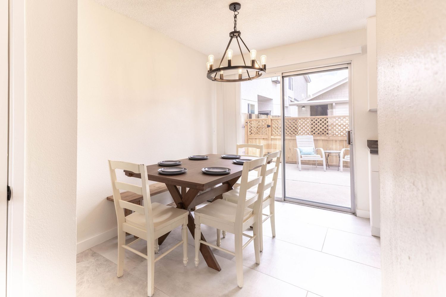 Bright dining area with round wood table, white chairs, chandelier, and sliding glass door to patio.