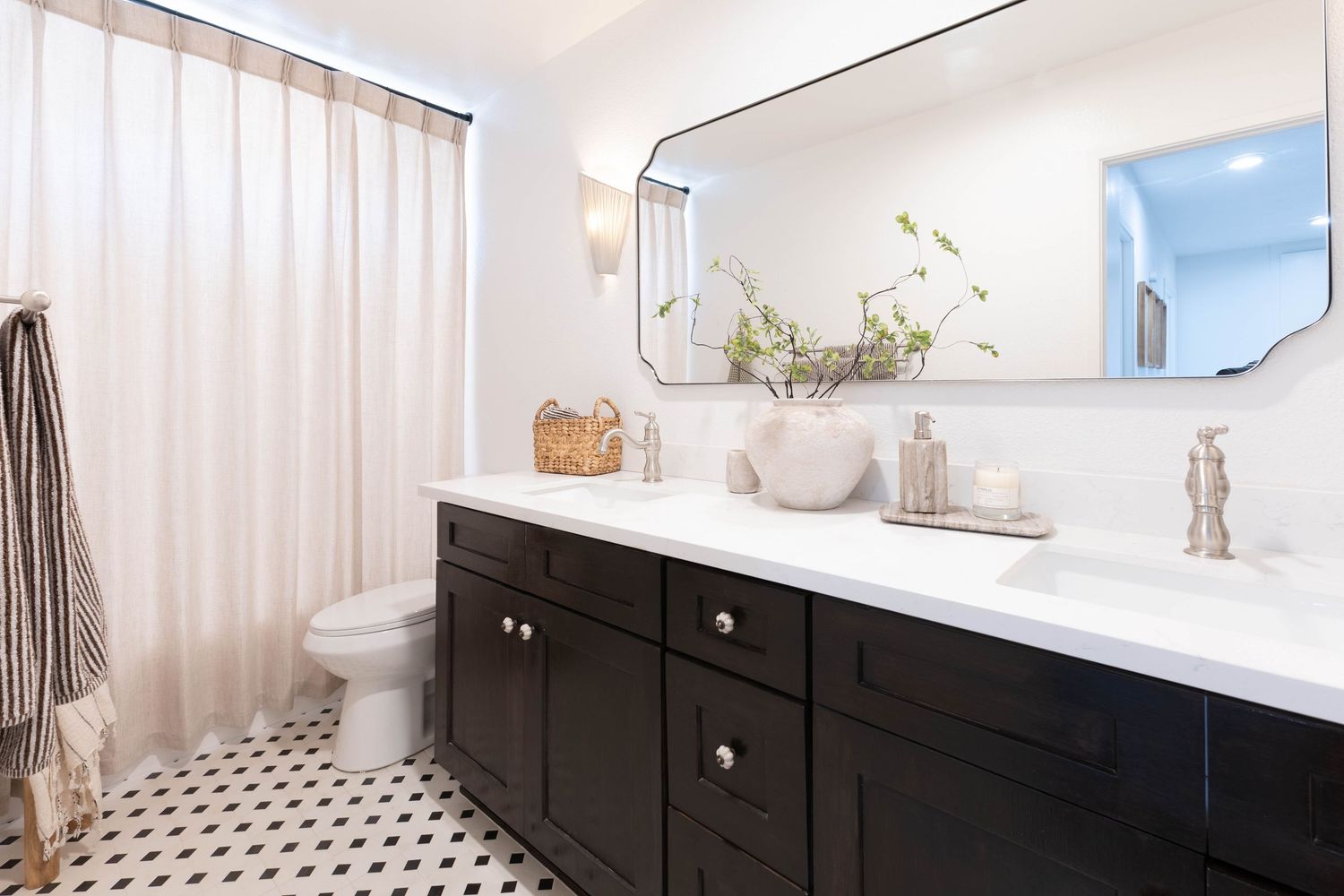 Modern bathroom with black vanity, white countertop, large mirror, vessel sink, and black-and-white patterned tile floor.