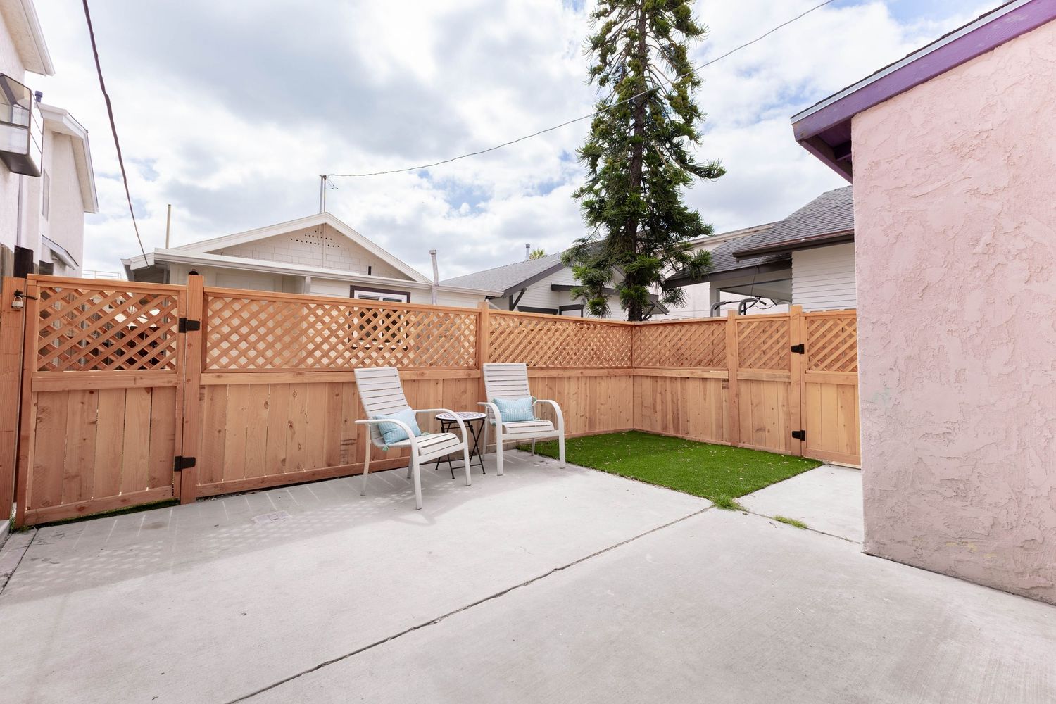 Private backyard patio with wooden lattice fence, two white chairs, and small green lawn area.