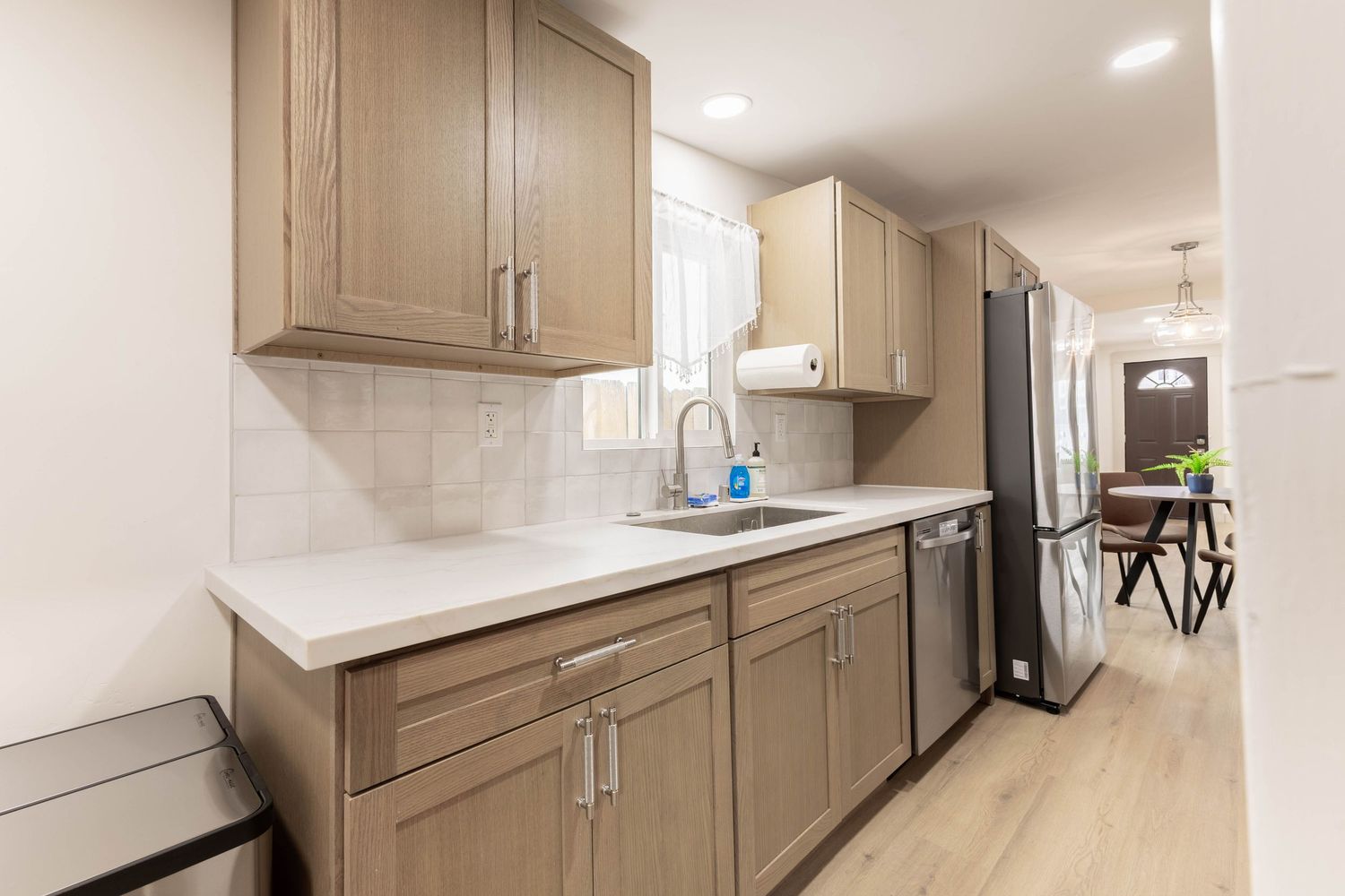 Modern kitchen with tan shaker cabinets, quartz countertops, stainless steel fridge, and hardwood floors.