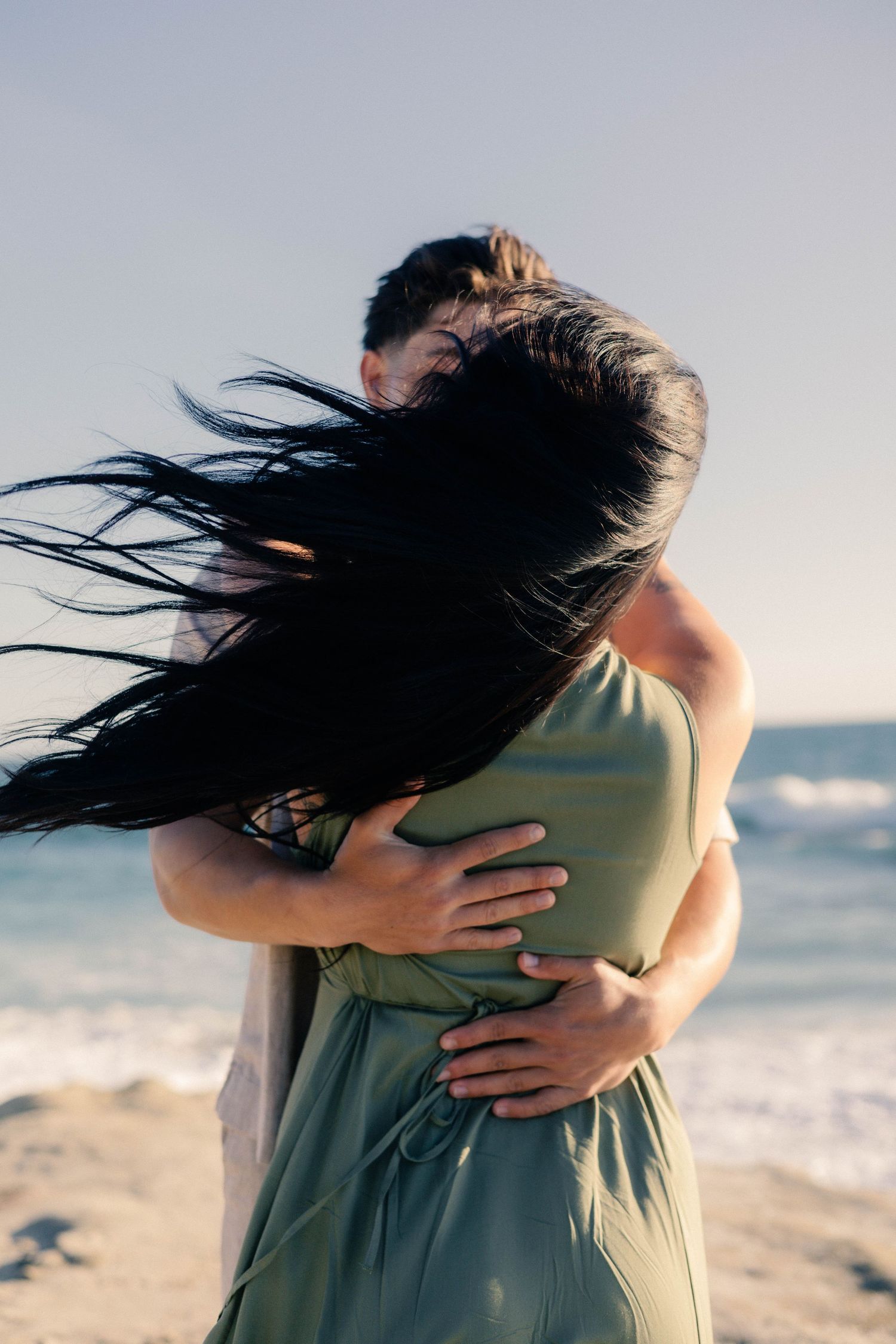 Couple sharing a close embrace on the beach, womans long dark hair blowing in the wind.