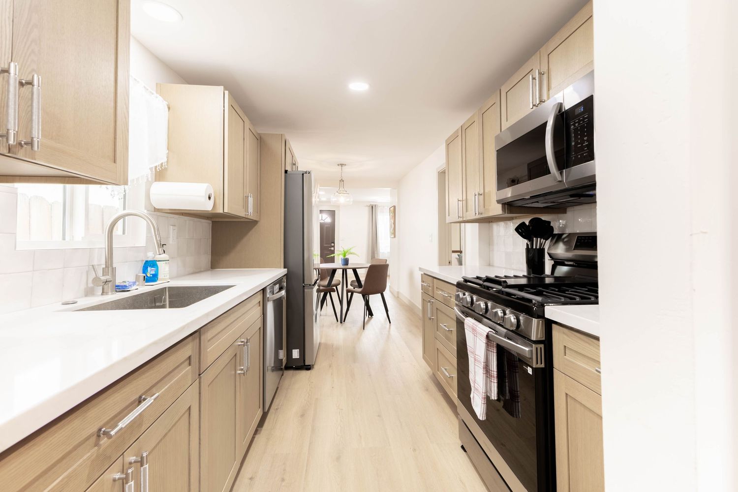 Modern galley kitchen with light wood cabinets, stainless steel appliances, and hardwood floors.
