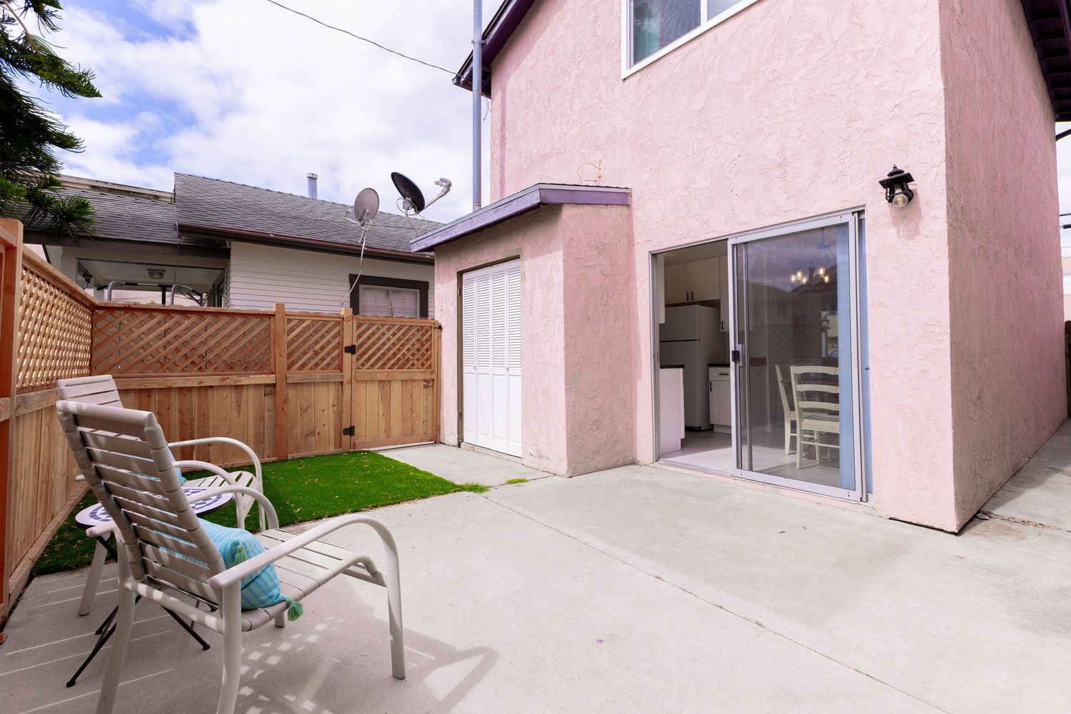 Pink stucco home exterior with sliding glass doors, patio chairs, artificial turf, and wooden privacy fence.