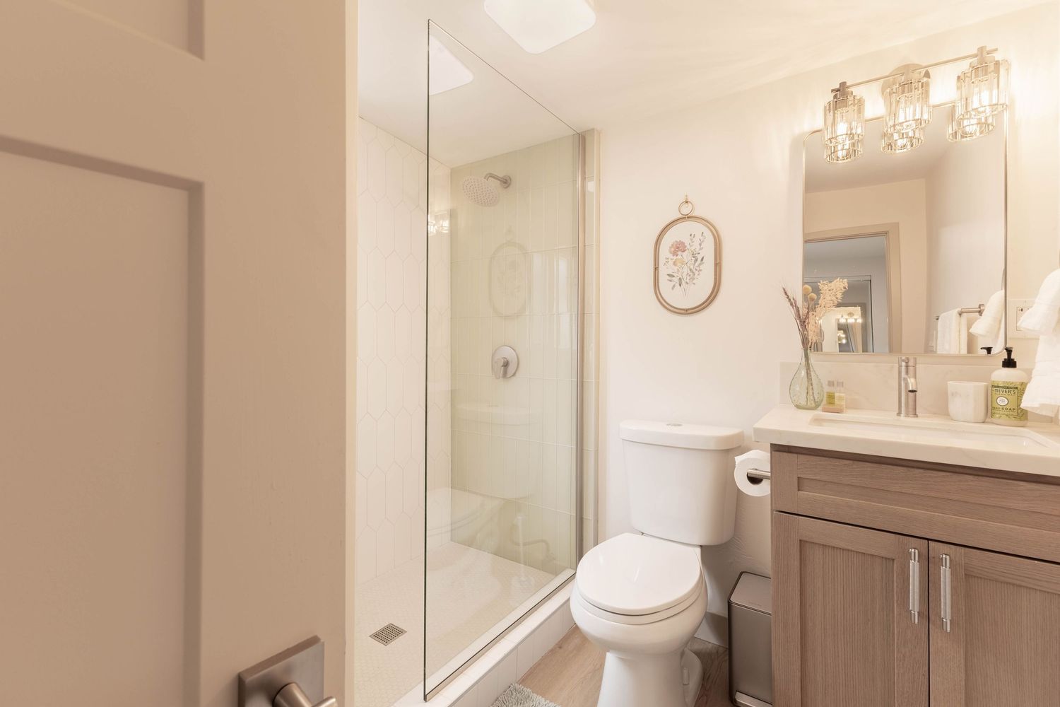 Modern bathroom with glass shower, wood vanity, white toilet, and warm lighting.