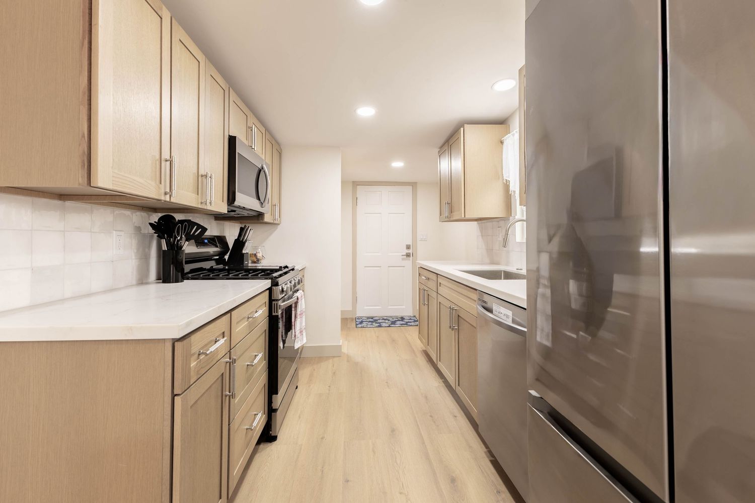 Modern kitchen with light wood cabinets, stainless steel appliances, white subway tile backsplash, and light hardwood floors.
