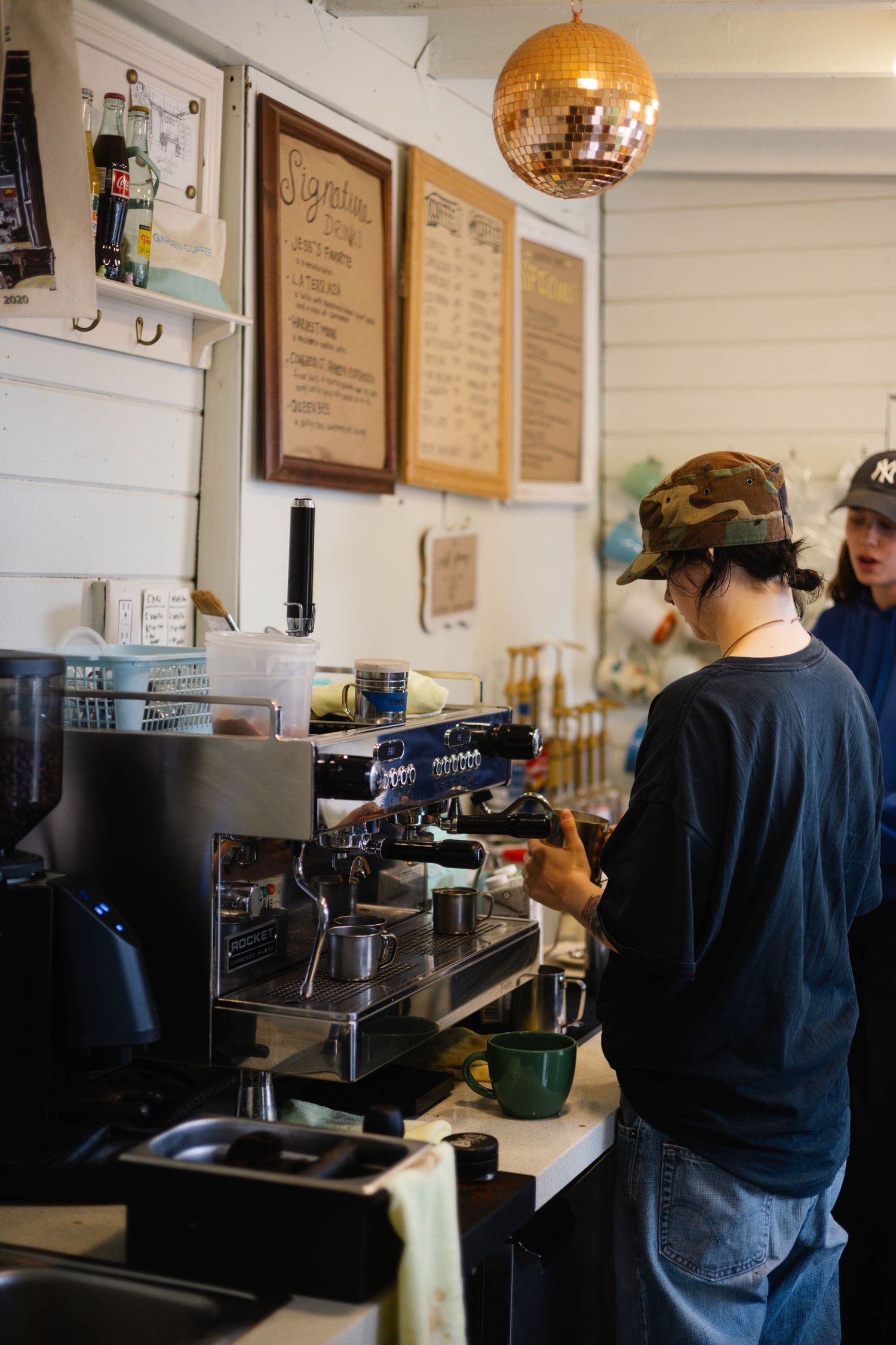 Barista operating espresso machine under a disco ball in a vintage coffee shop.