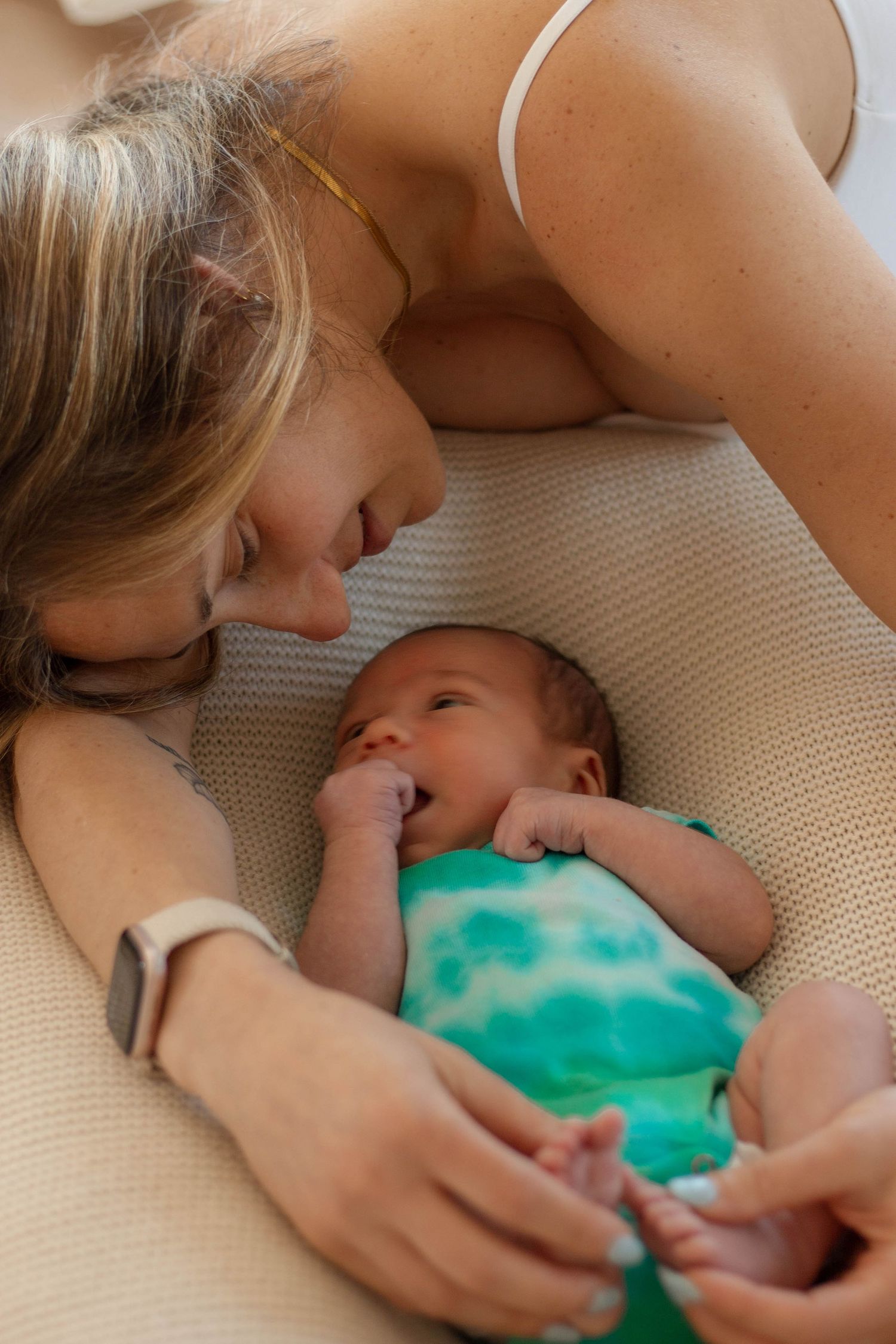 Mother lovingly gazing at her newborn baby resting on a textured pillow in a tender bonding moment.