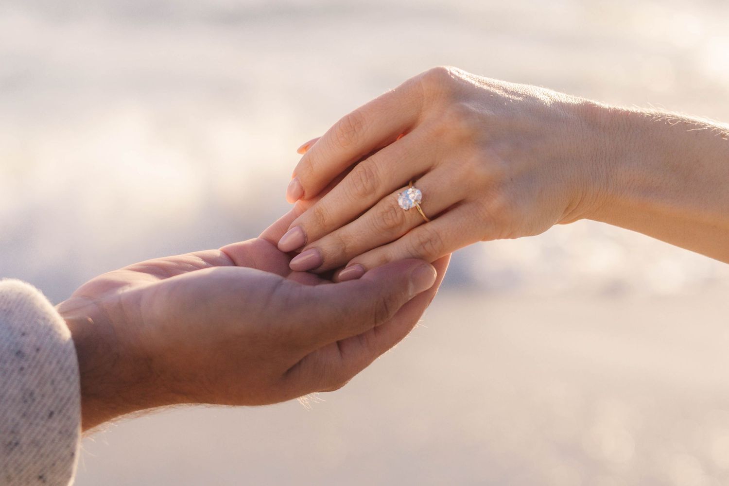 Close-up of an engagement ring on a woman's hand held by her partner at the beach.