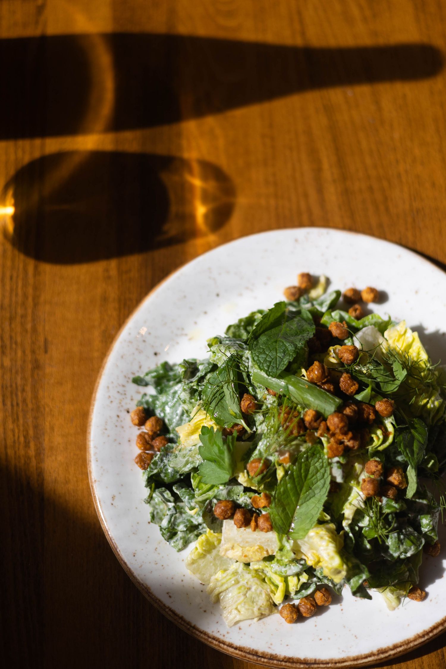 Fresh green salad with roasted chickpeas and mint leaves on a white plate, served on a wooden table.