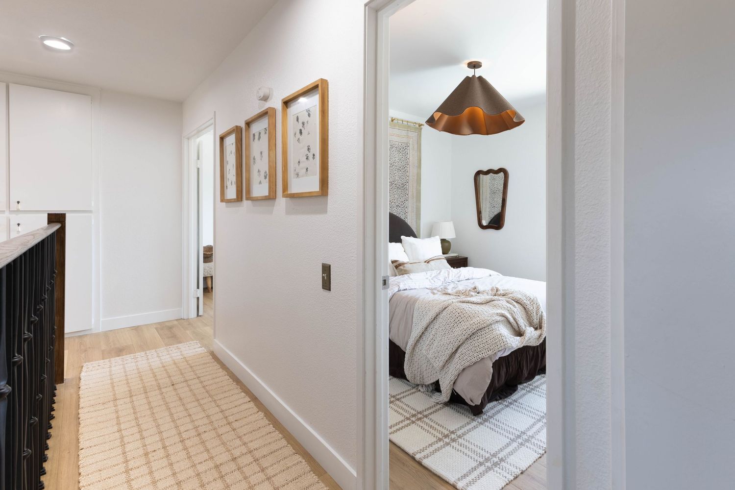Bright hallway with checkered tile floor leading to a cozy bedroom with white bedding and a copper pendant light.