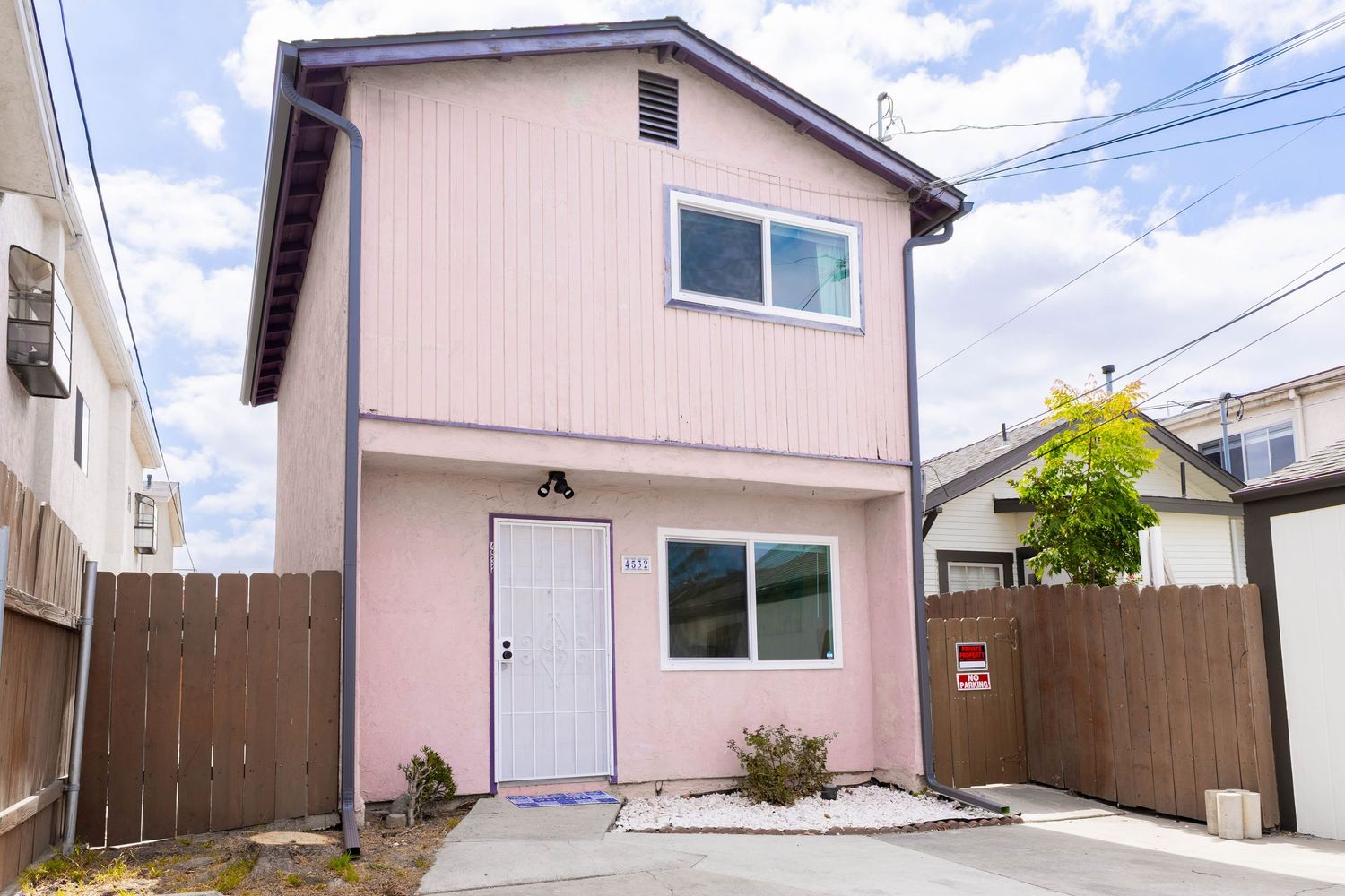 Two-story pink exterior home with white front door, wood fence, and small concrete pathway.