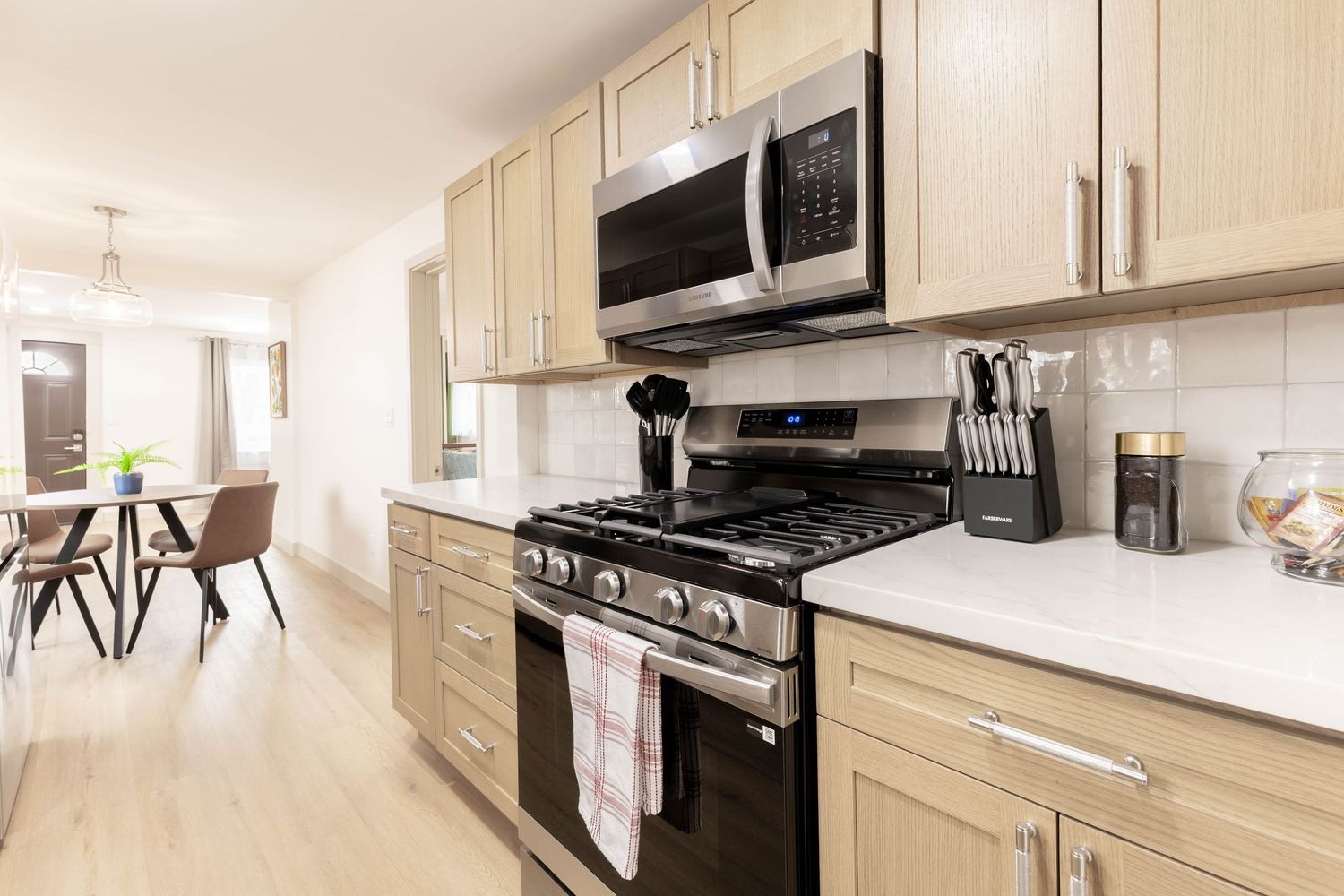 Modern kitchen with light wood cabinets, stainless steel appliances, gas range, and white quartz countertops.