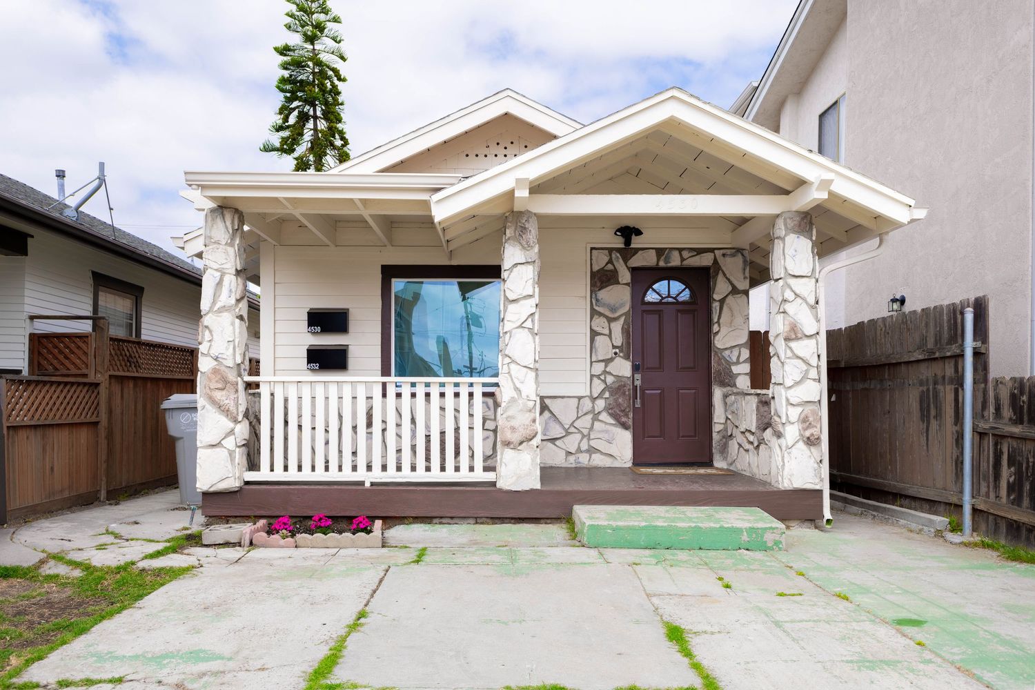 Charming bungalow home exterior with stone columns, white porch railing, and purple front door on concrete driveway.