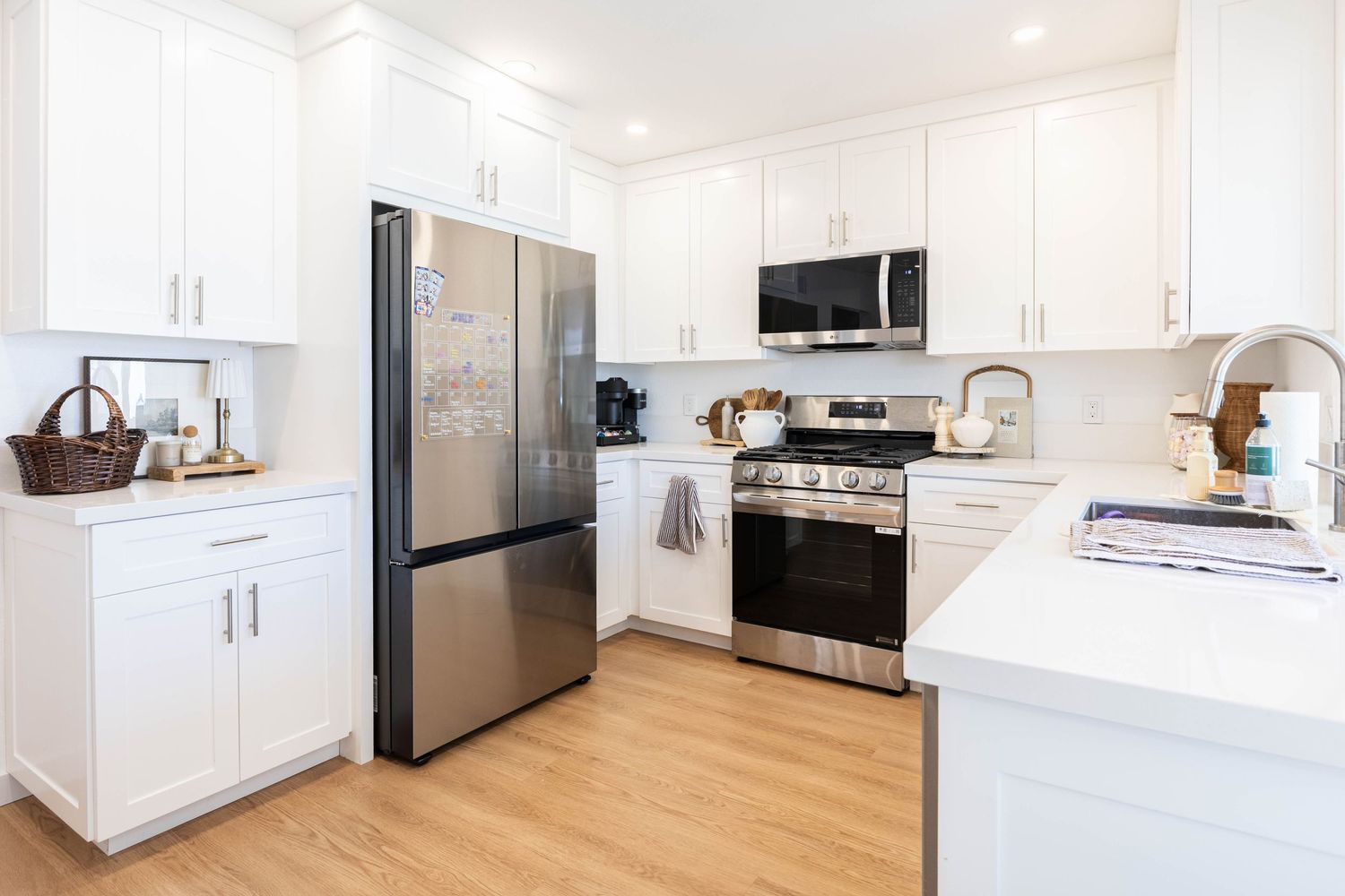 Modern white kitchen with stainless steel appliances, shaker cabinets, quartz countertops, and light hardwood floors.