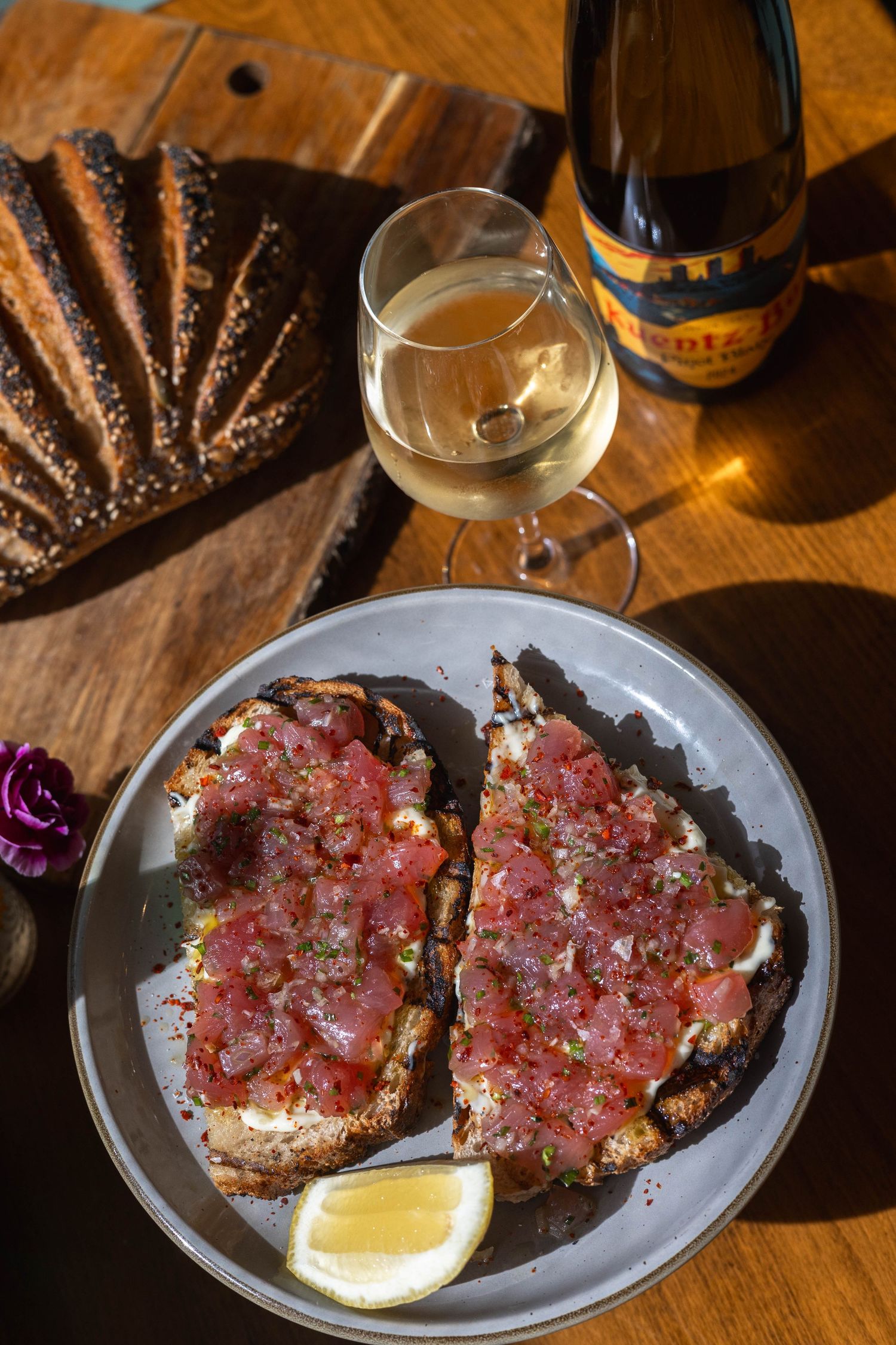 Dark bread topped with tuna tartare served on a plate with lemon wedge, paired with a glass of white wine.
