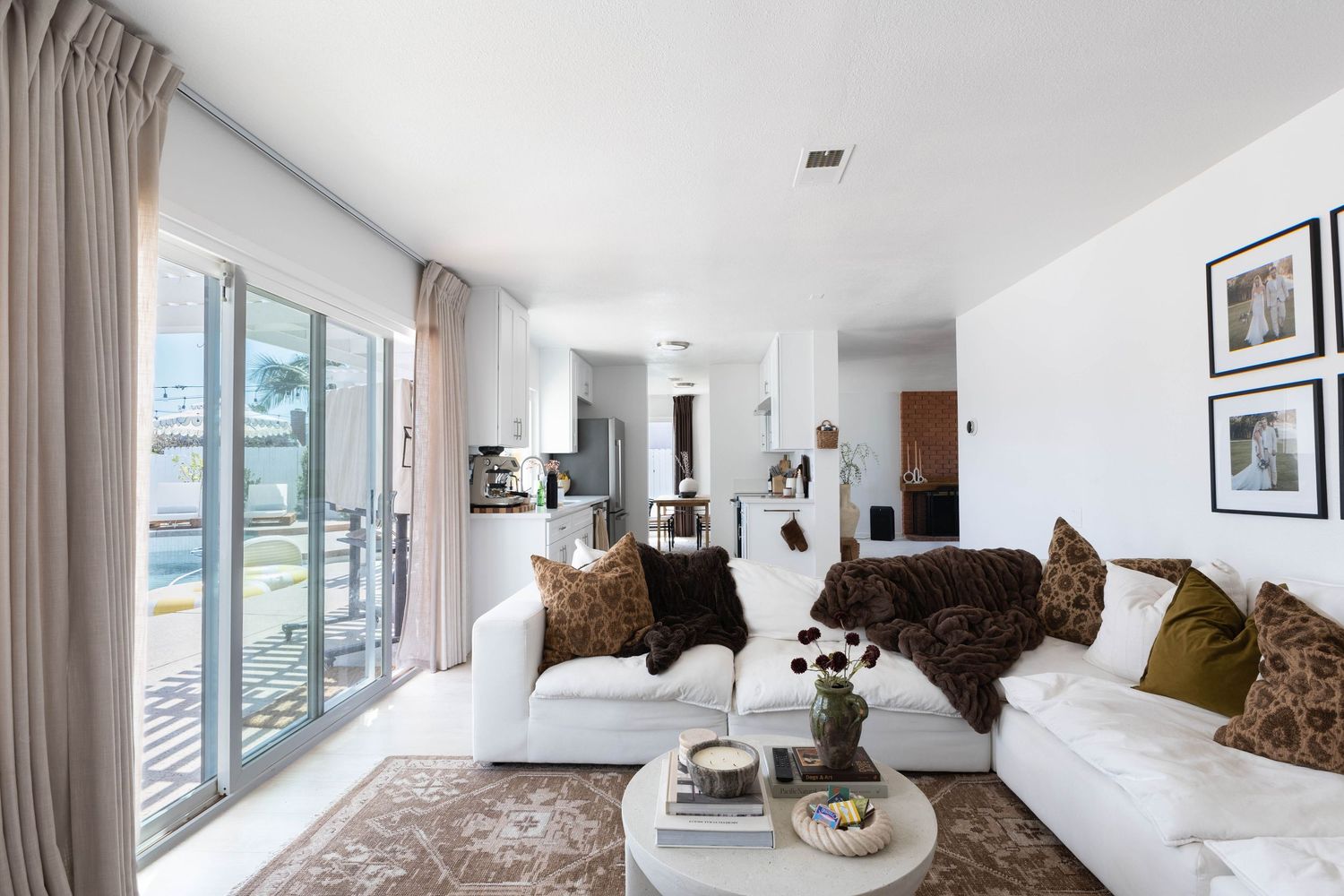 Bright modern living room with white sofas, brown fur throw, green pillows, patterned rug, and sliding glass doors to balcony.
