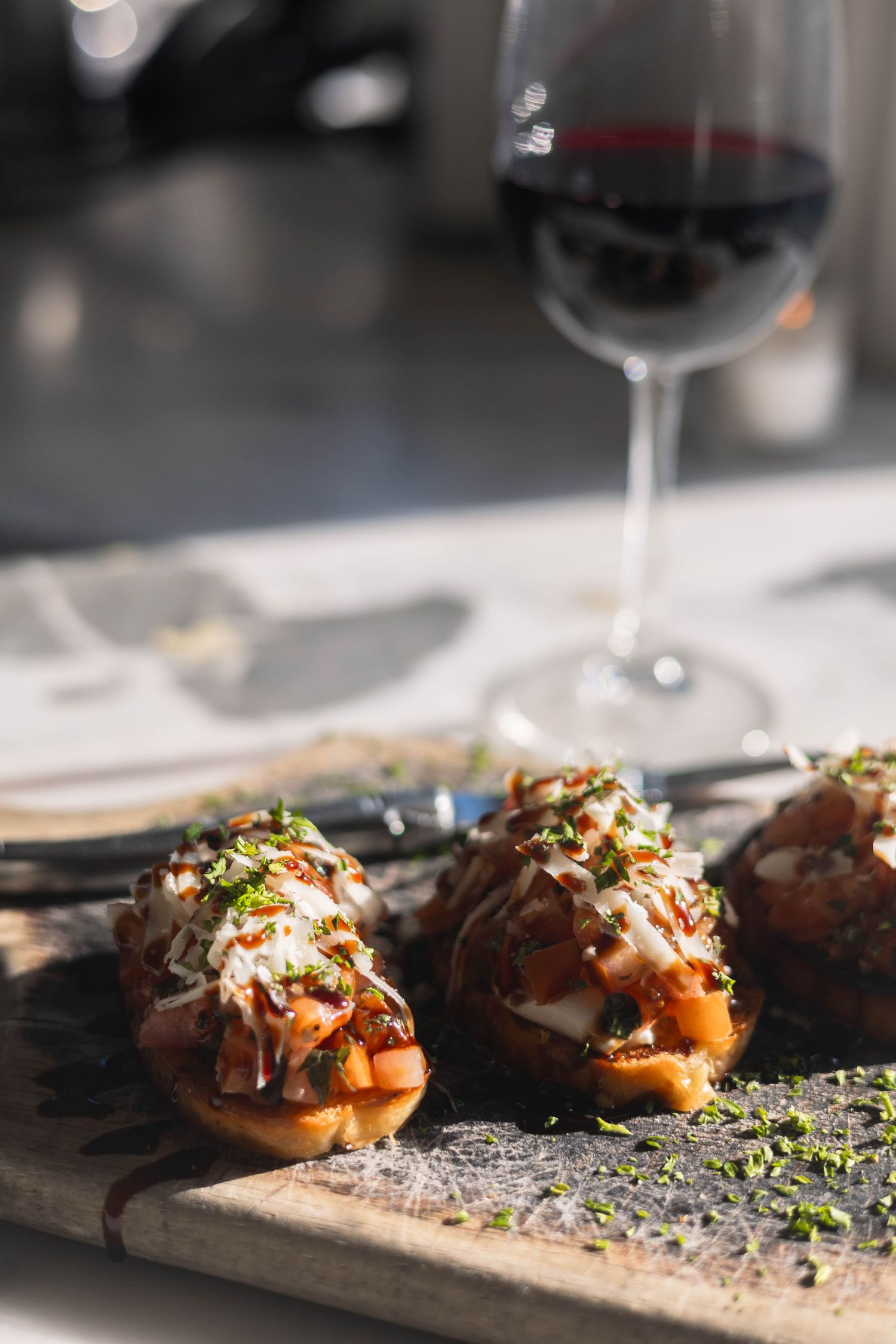 Bruschetta topped with tomatoes, cheese, and herbs on a wooden board with a glass of red wine in the background.
