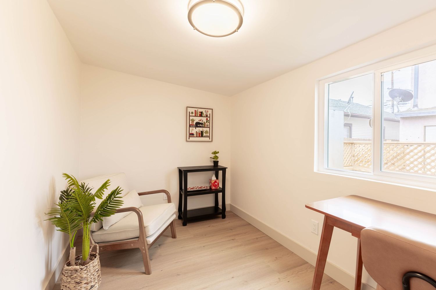 Small bright room with light wood floors, single chair, black shelving unit, desk, and a window with natural light.