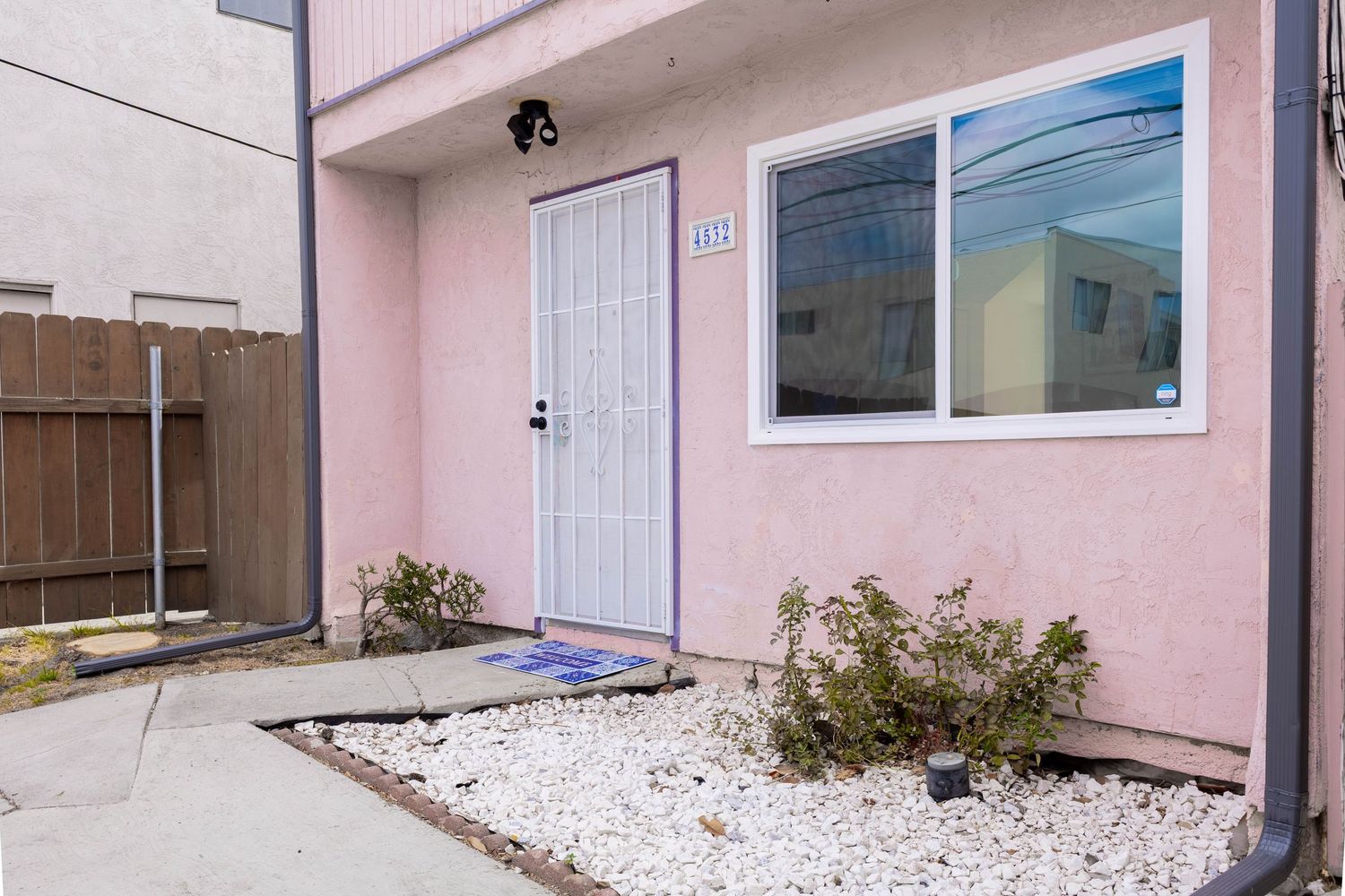 Pink exterior home entrance with white door, security light, and decorative white rock landscaping.