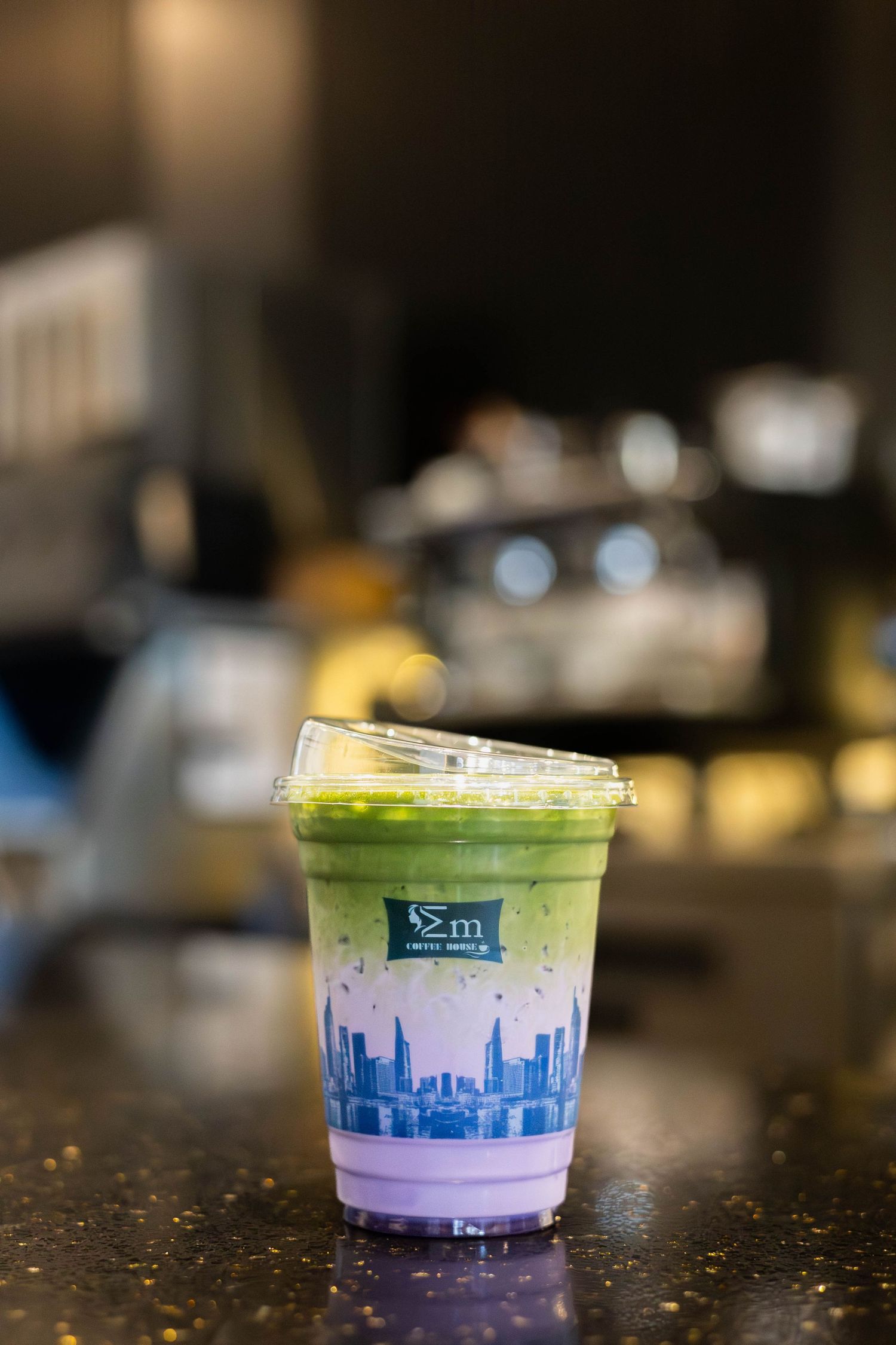 A vibrant matcha latte in a decorative cup with a city skyline design sits on a dark cafe counter.