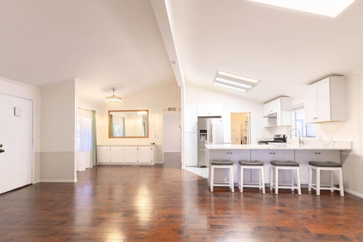 Open-concept kitchen and living area with white cabinets, bar seating, skylights, and rich hardwood floors.
