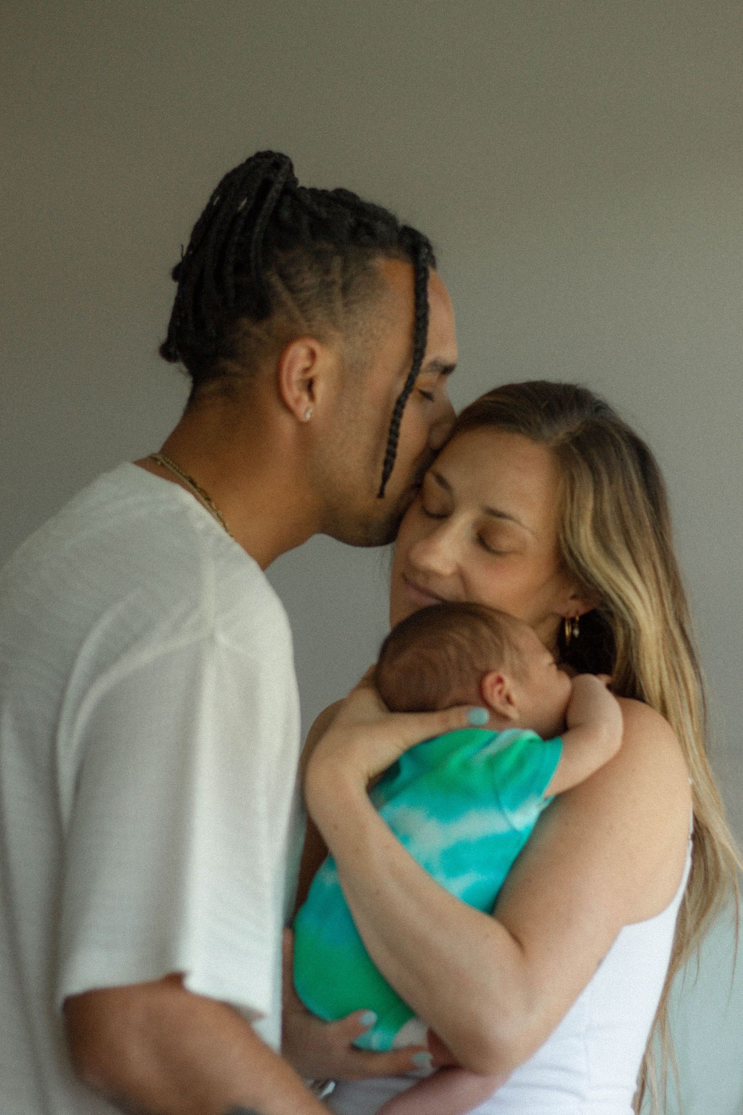 A couple shares a tender moment as the man kisses the woman on the cheek while she holds their newborn baby.