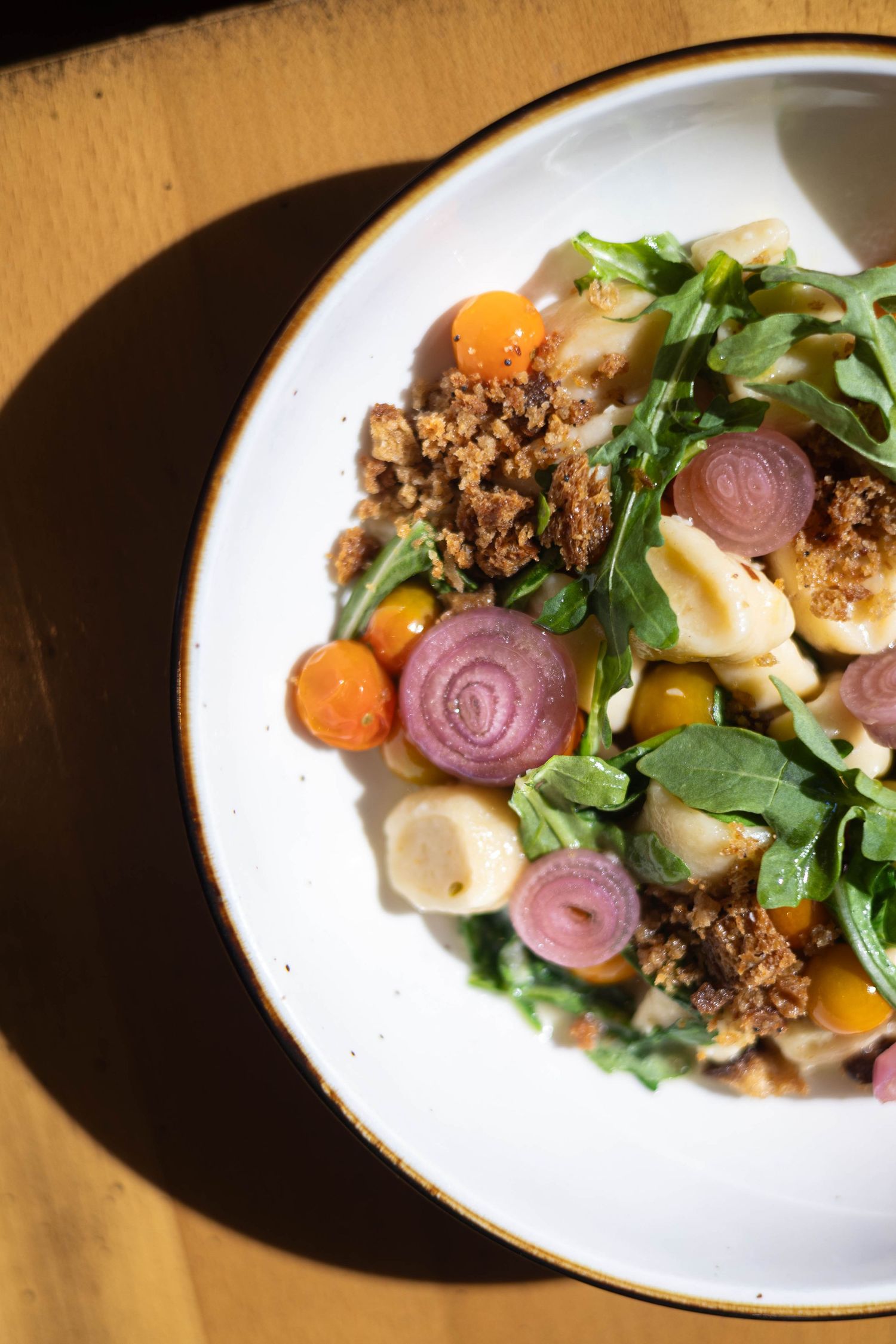 Fresh orecchiette pasta salad with arugula, cherry tomatoes, red onion, carrots, and breadcrumbs on a white plate.