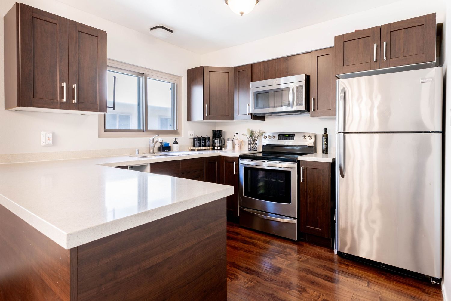 Modern kitchen with dark wood cabinets, stainless steel appliances, white quartz countertops, and hardwood floors.