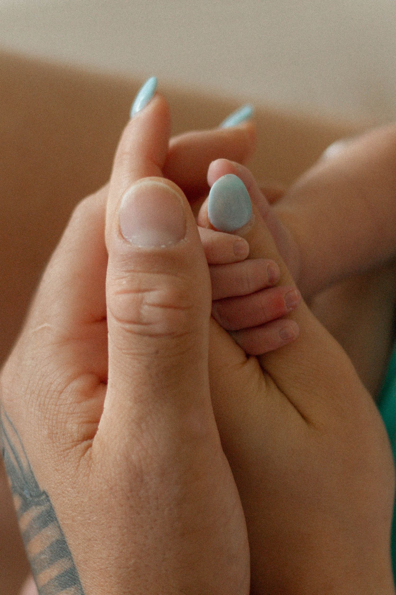 Close-up of a mother's hand with light blue nail polish gently holding a newborn baby's tiny feet.