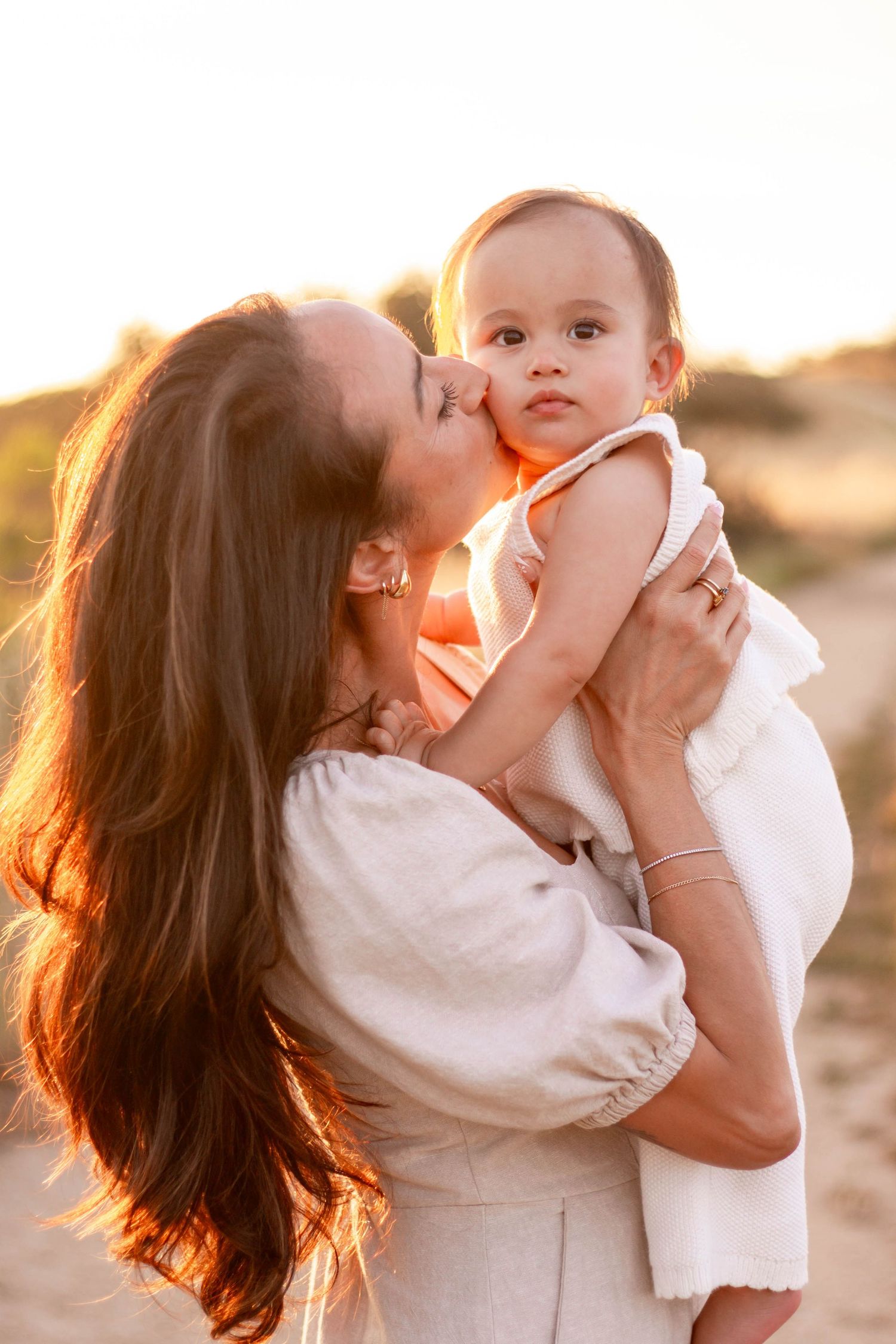Mother kissing her baby's cheek during a golden sunset outdoor photo session.