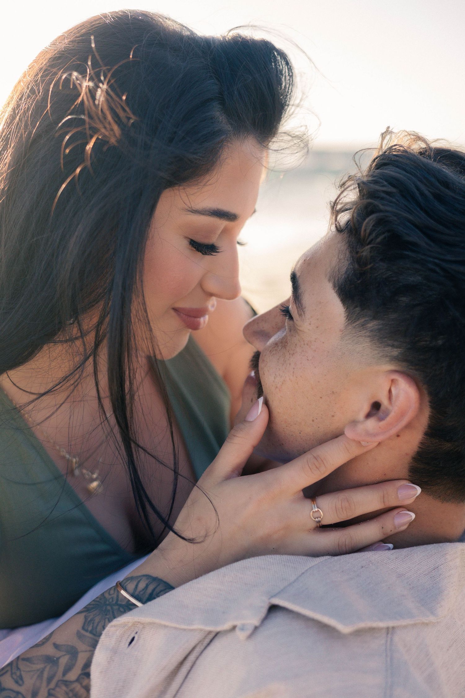 Intimate close-up of couple about to kiss on beach, woman gently cupping mans face in warm light.